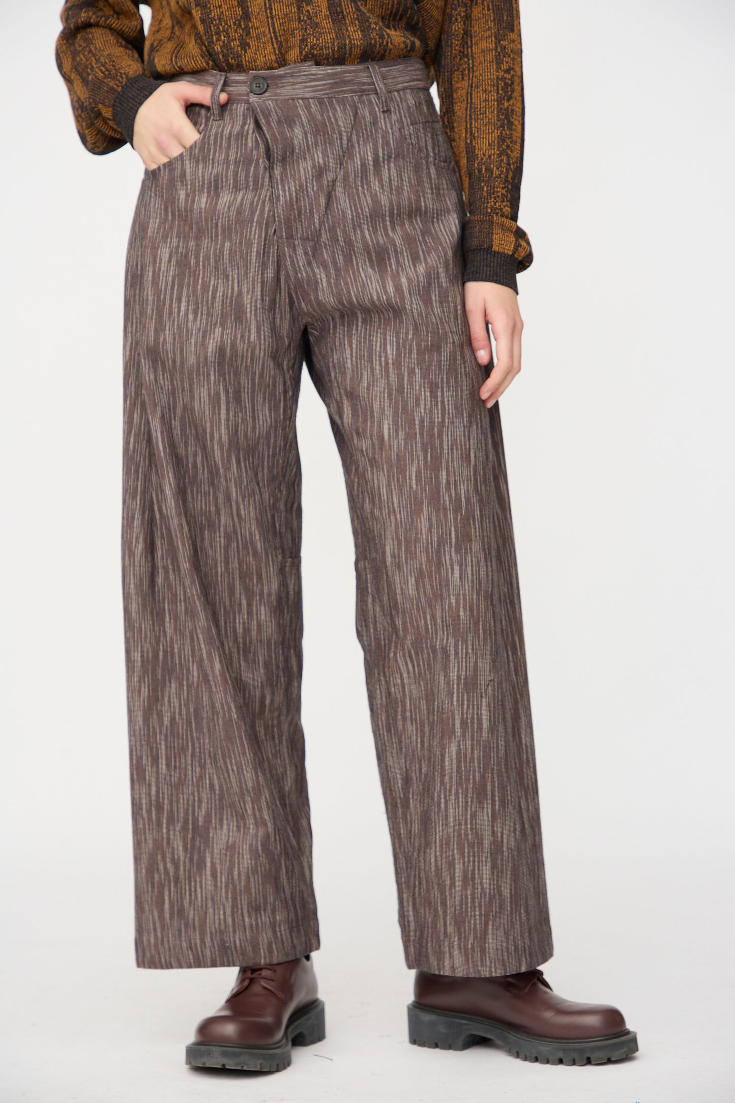 Person wearing Jan-Jan Van Essche Kasuri Cotton Silk Trousers #90 in Old Lavender, paired with a brown and black sweater and dark brown platform boots, standing against a plain light background.