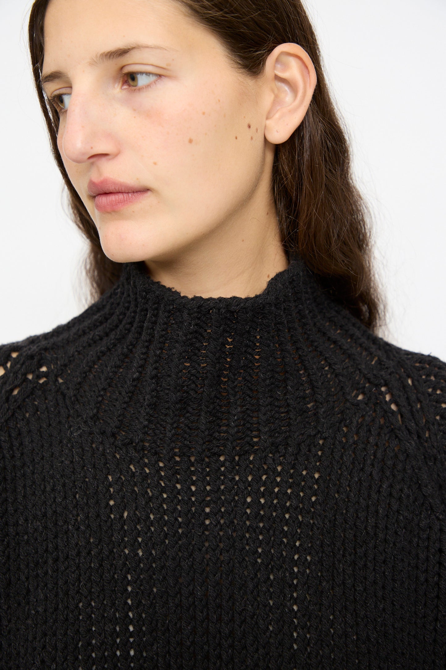 A person with long brown hair wears the Jan-Jan Van Essche Lalin Knit #68 Sweater in Pitch Black, looking to the side against a plain background.