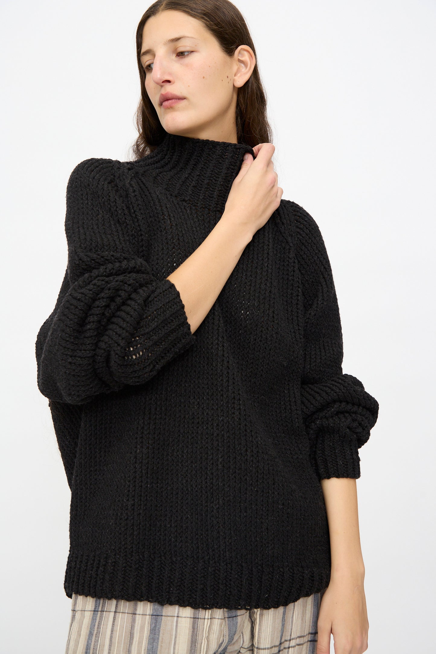 A woman wears the Jan-Jan Van Essche Lalin Knit #68 Sweater in Pitch Black with striped pants, standing against a plain white background.