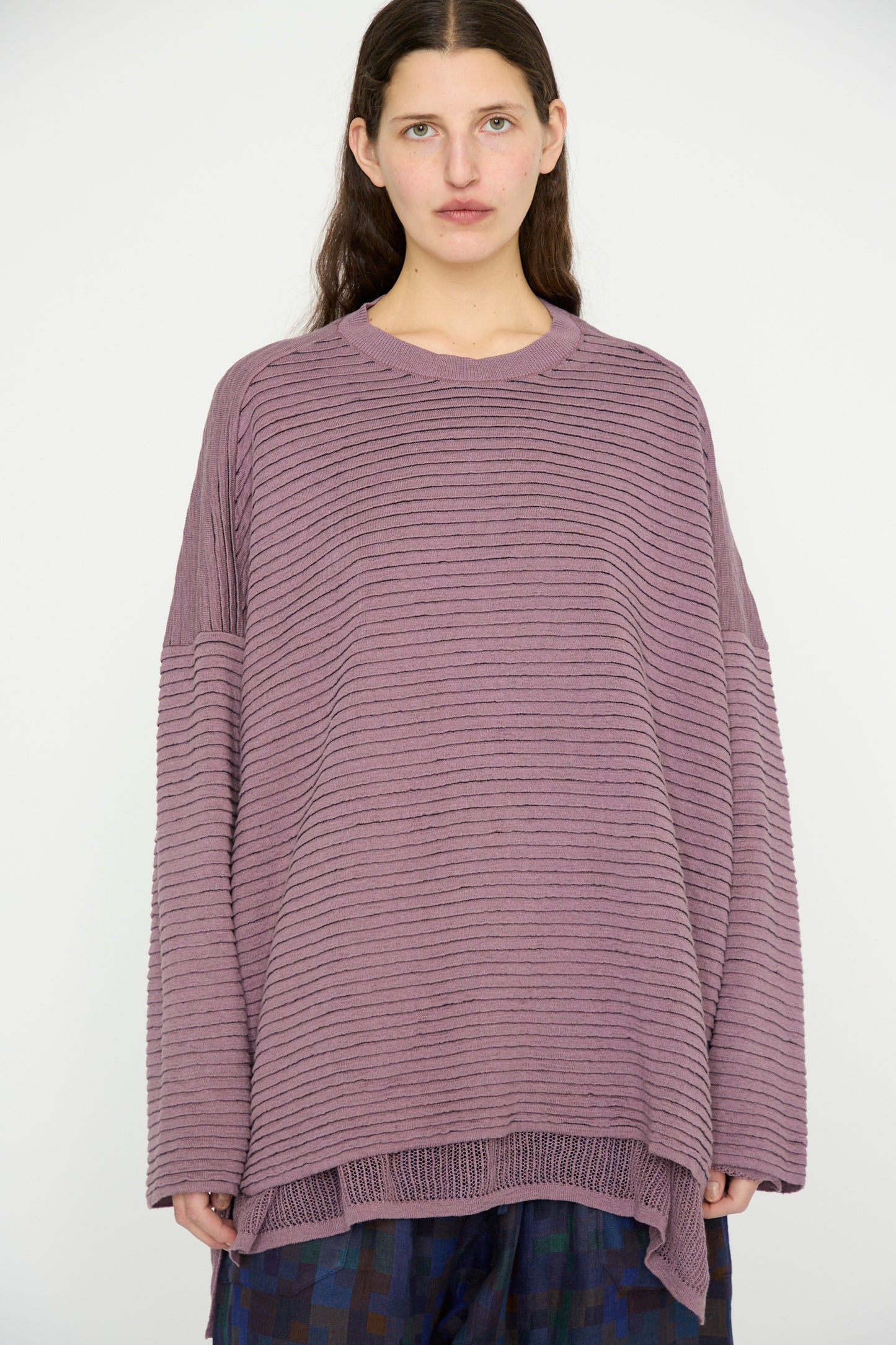 A person with long hair wears the oversized Lavender Linen Cotton Yarn Knit #70 sweater by Jan-Jan Van Essche, paired with a patterned skirt against a plain background.