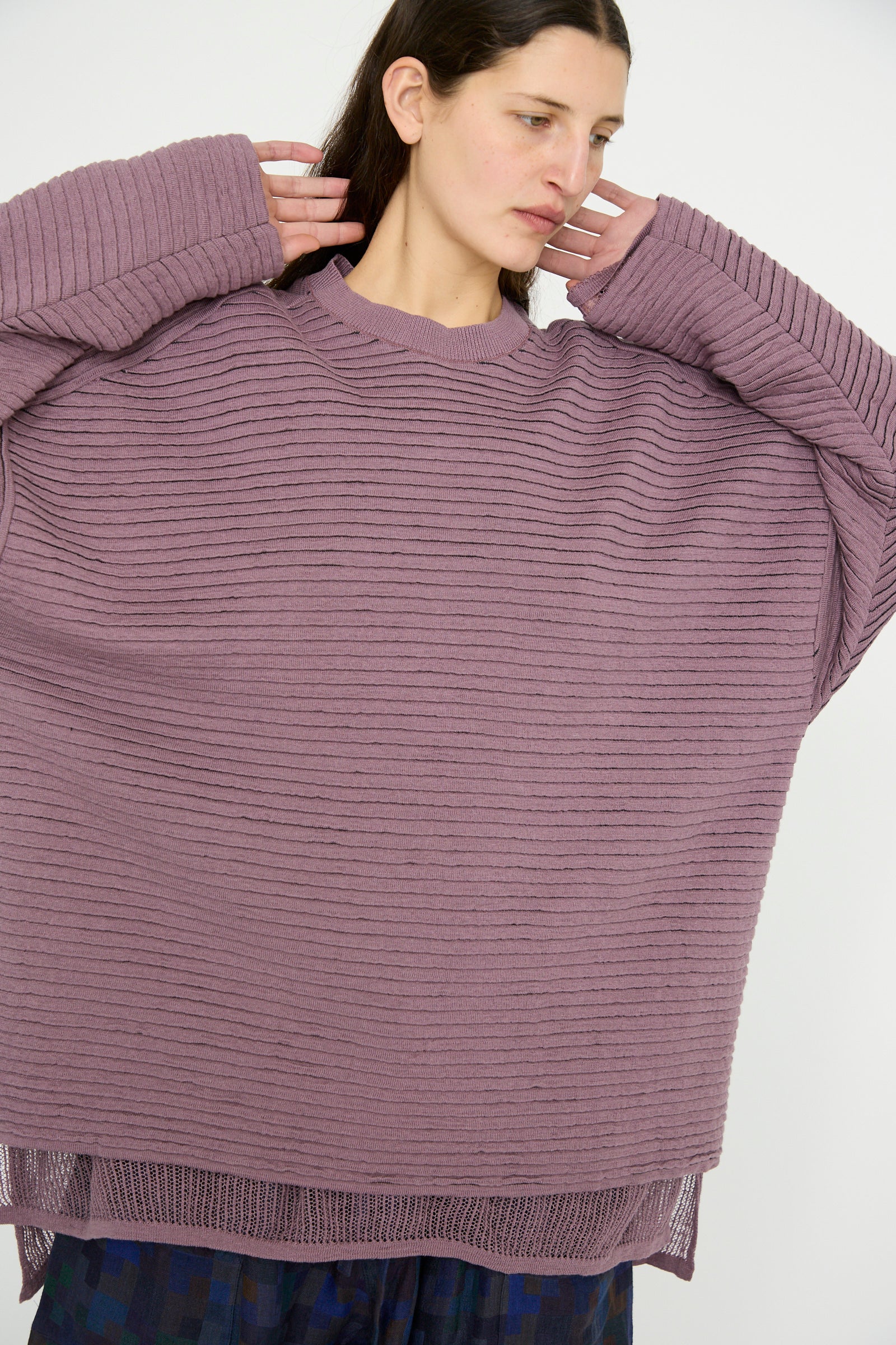 A person adjusts the collar of a Jan-Jan Van Essche Linen Cotton Yarn Knit #70 in Lavender, an oversized ribbed sweater with long sleeves featuring a delightful striped texture.