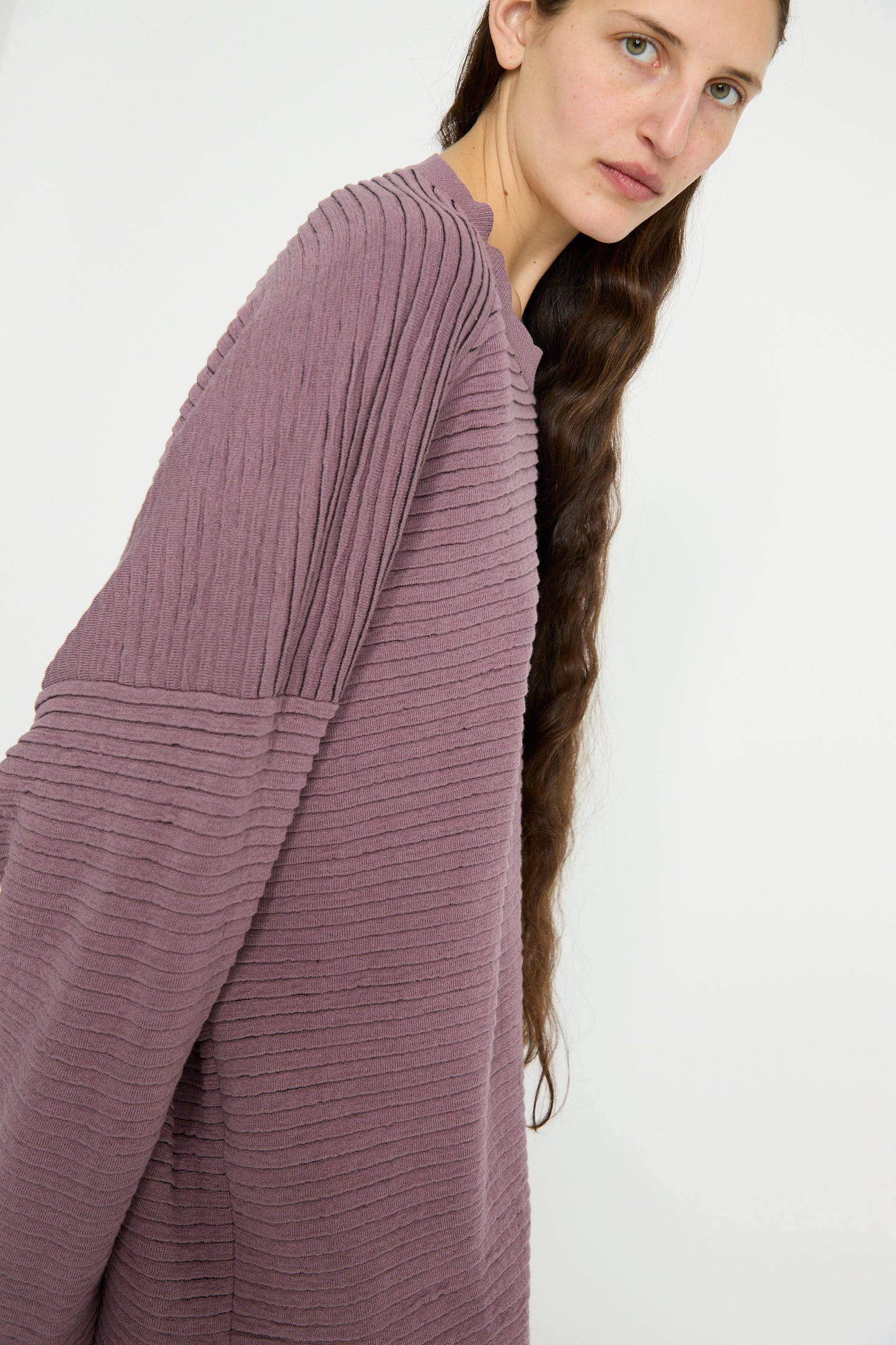 With long hair and a blank backdrop, a person wears an oversized Linen Cotton Yarn Knit #70 in Lavender by Jan-Jan Van Essche.