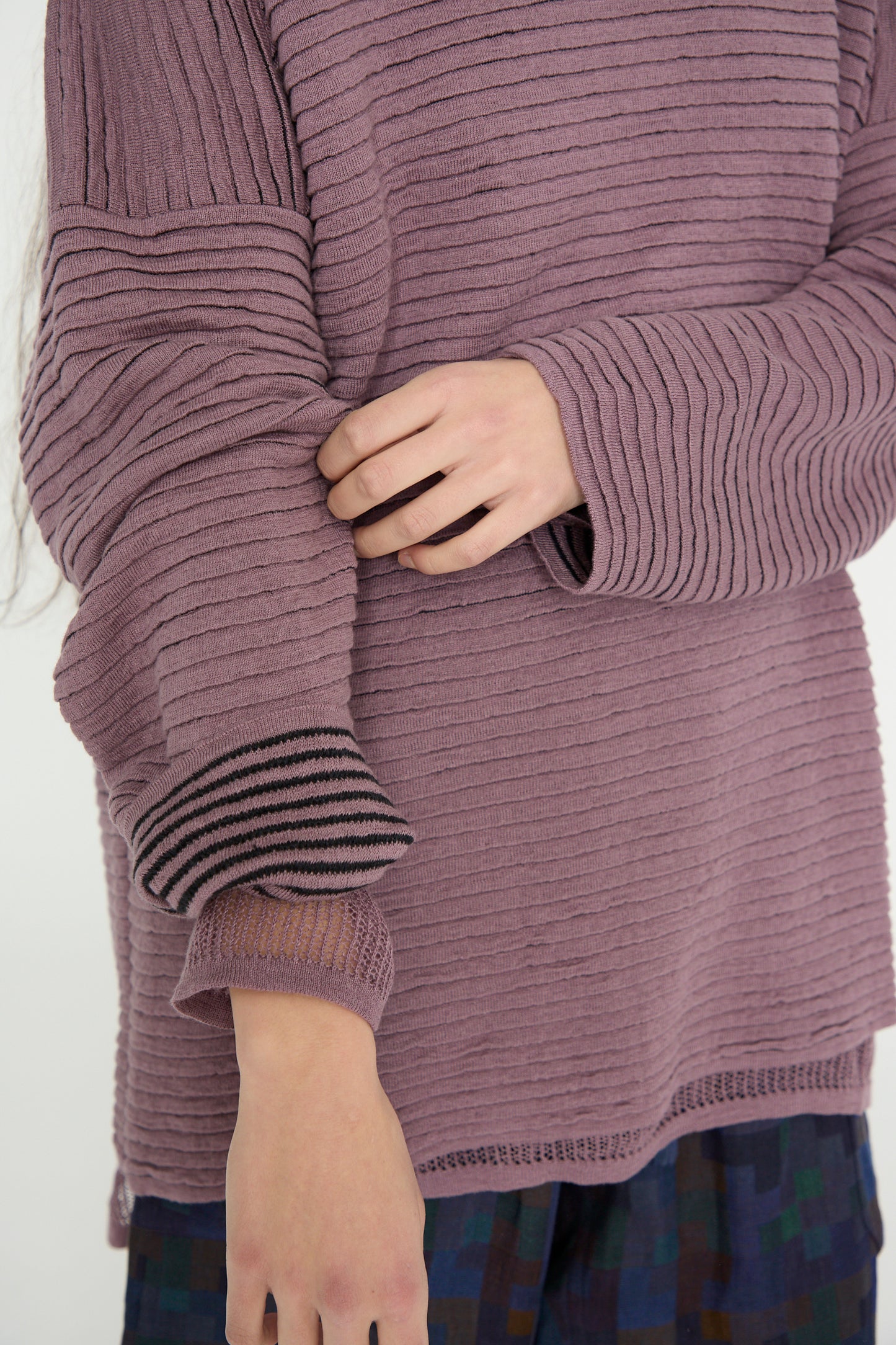 Someone in a Jan-Jan Van Essche Linen Cotton Yarn Knit #70 sweater in Lavender adjusts their sleeve, paired with plaid pants.