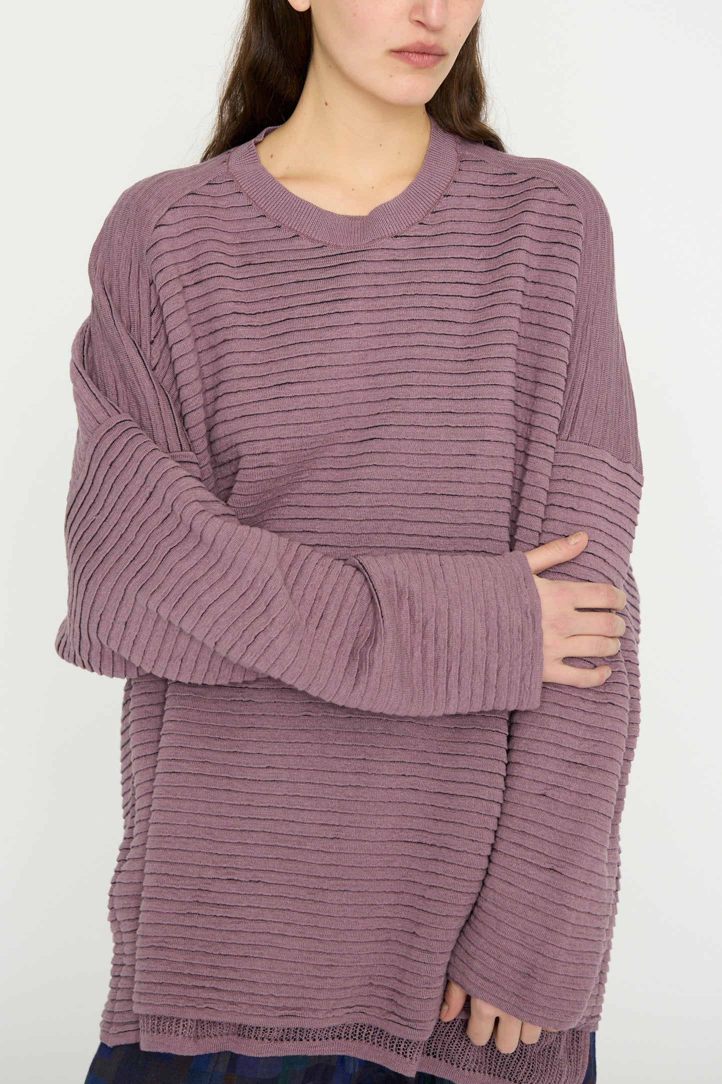 The person stands against a plain background, enveloped in Jan-Jan Van Essche’s oversized Linen Cotton Yarn Knit #70 in Lavender.