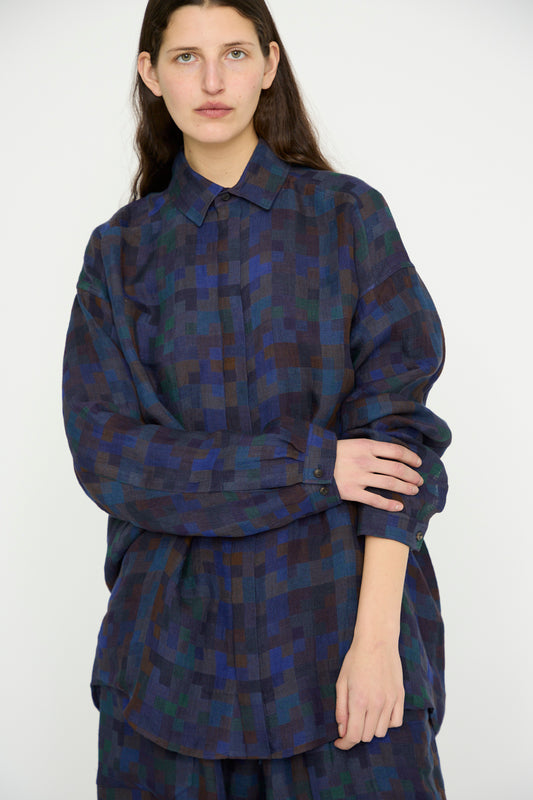 A person stands against a plain backdrop wearing Jan-Jan Van Essche's Linen Double Cloth Shirt #106 in Puzzle, an oversized long sleeve shirt featuring a soothing blue and green checkered pattern.