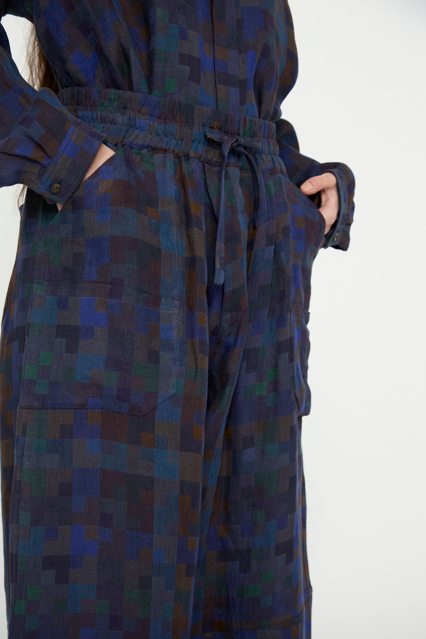 Wearing Jan-Jan Van Essche's Linen Double Cloth Trouser #86 in Puzzle, a person displays a mix of dark blue, green, and brown square patterns with their hands in pockets.