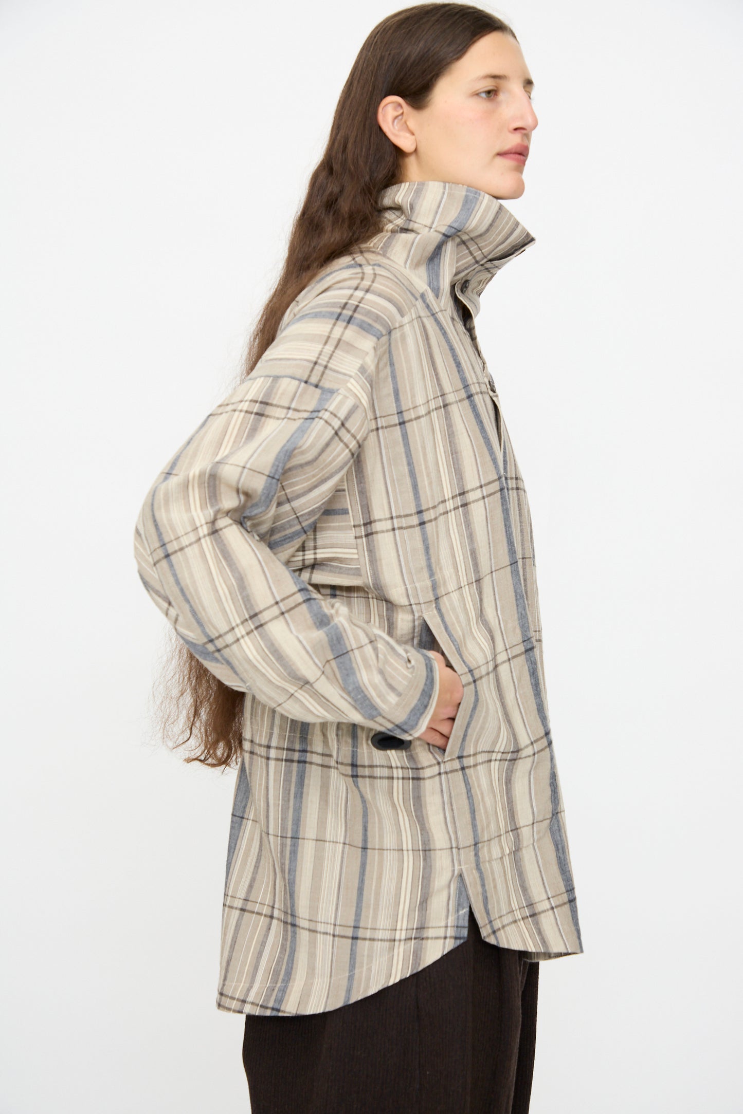 A person stands in profile, hands in pockets, wearing the Jan-Jan Van Essche Madras Plaid Shirt #110 in Plaster—a gray plaid shirt jacket—against a plain white background.