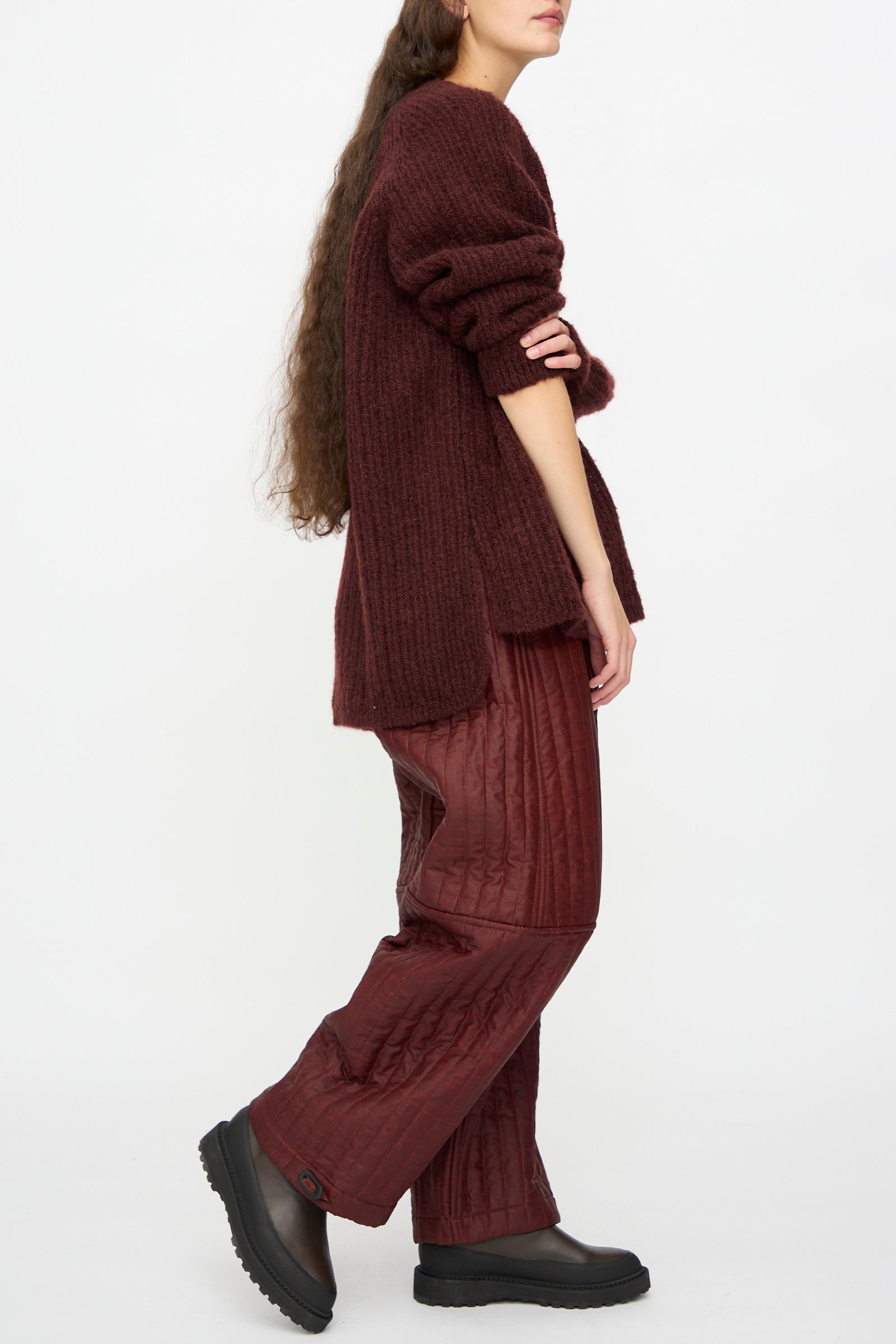 A person wears the Jan-Jan Van Essche Mohair Knit #71 Sweater in Oxblood, quilted maroon pants, and black platform shoes while standing against a plain white background.
