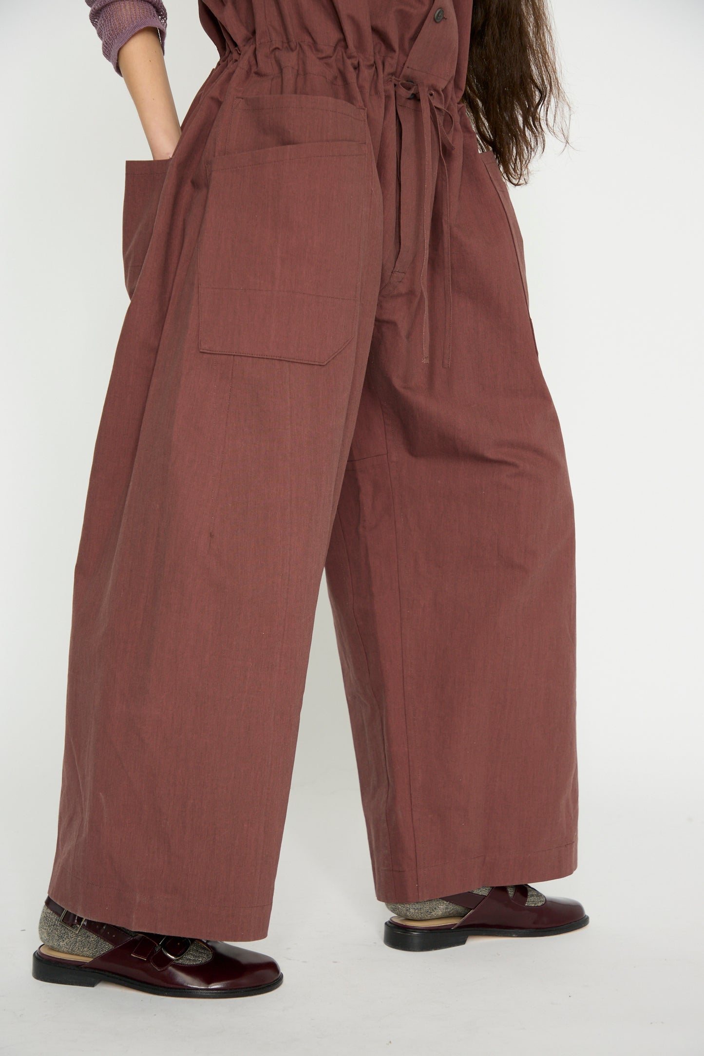 Person wearing the Jan-Jan Van Essche Oxford Cloth Jumpsuit #12 in Prune and brown shoes with socks.