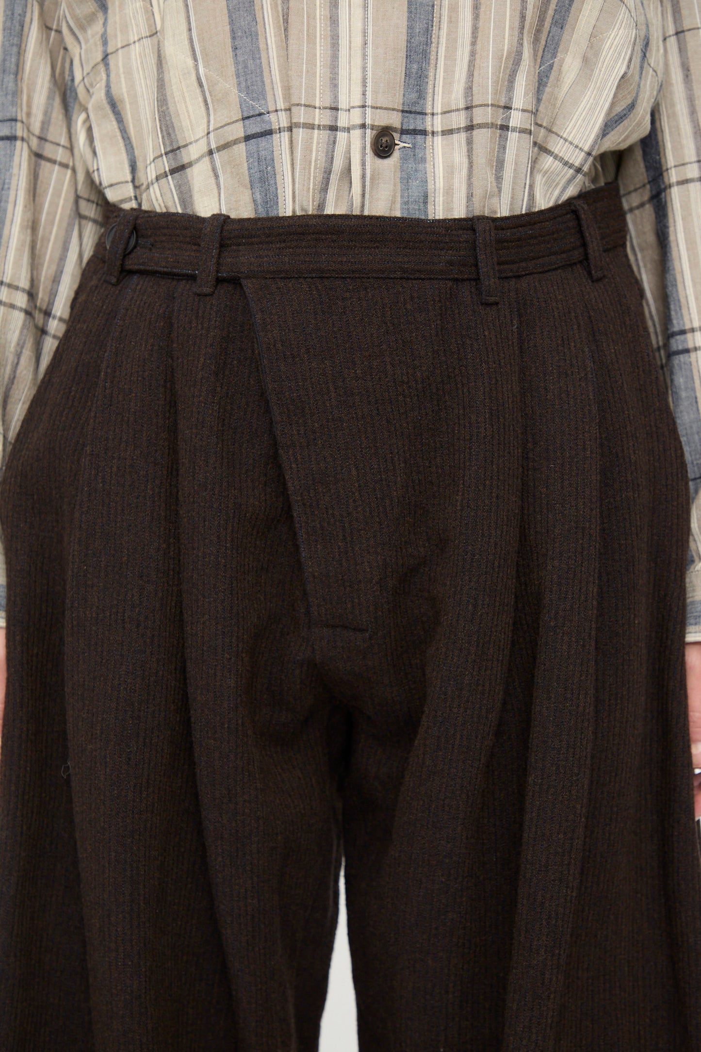 A person wearing a beige and gray striped shirt tucked into Jan-Jan Van Essche Ridged Linen Wool Trousers #87 in Indigo and Eggplant, featuring high-waisted, wide-leg pleated design for a relaxed fit.