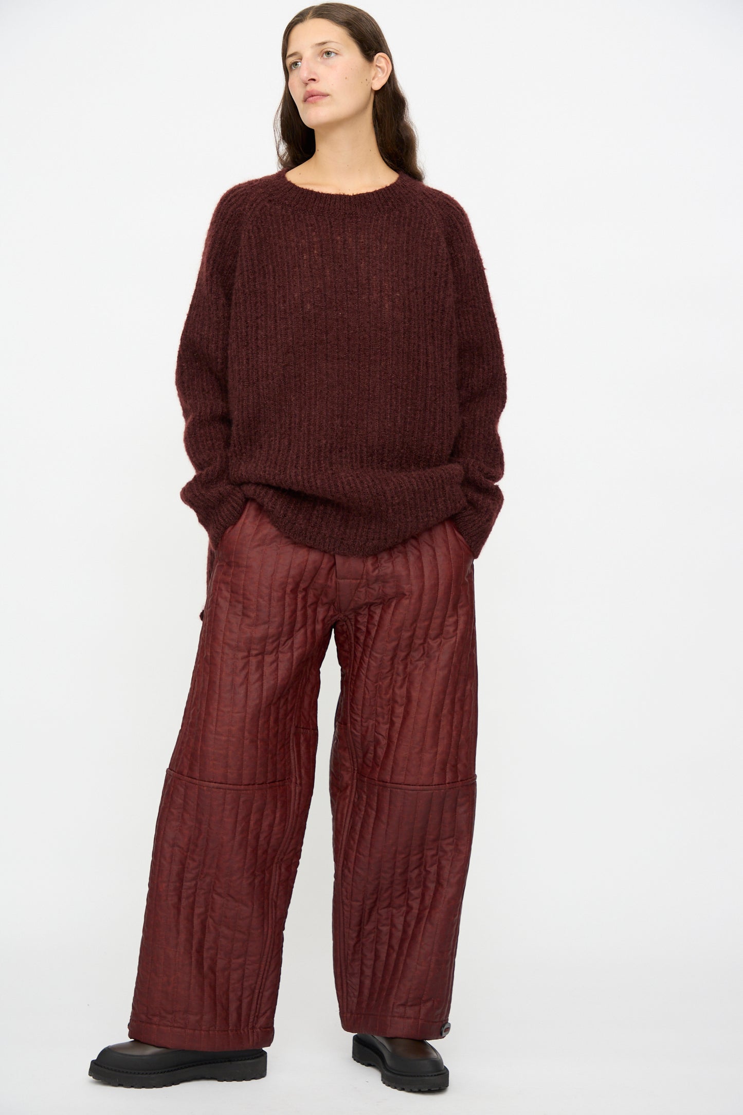 A person wears Jan-Jan Van Essche Shuliang Silk Padded Trousers #89 in Oxblood with a loose dark maroon sweater and black shoes, standing against a plain white background.