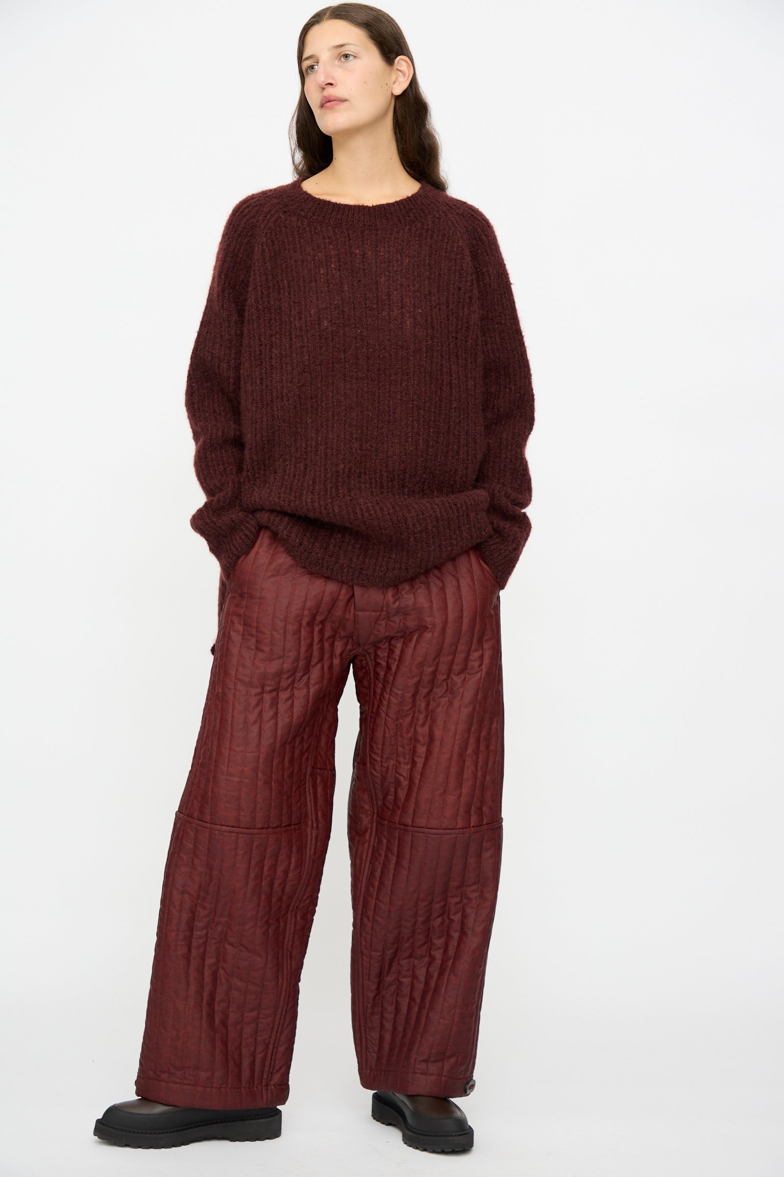 A person wears Jan-Jan Van Essche Shuliang Silk Padded Trousers #89 in Oxblood with a loose dark maroon sweater and black shoes, standing against a plain white background.