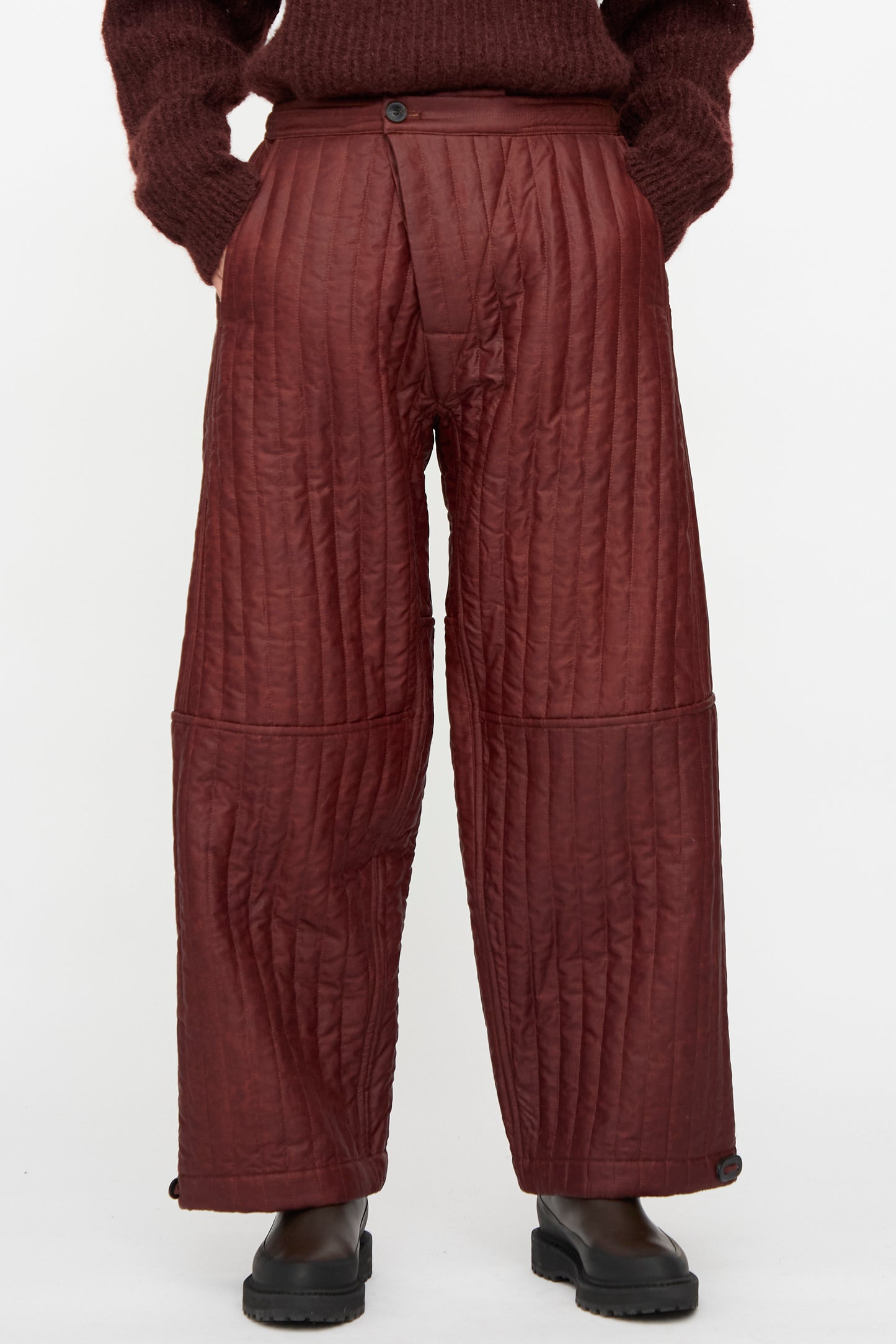 A person wears Jan-Jan Van Essche Shuliang Silk Padded Trousers #89 in Oxblood with a matching maroon sweater and black boots, standing against a plain white background.