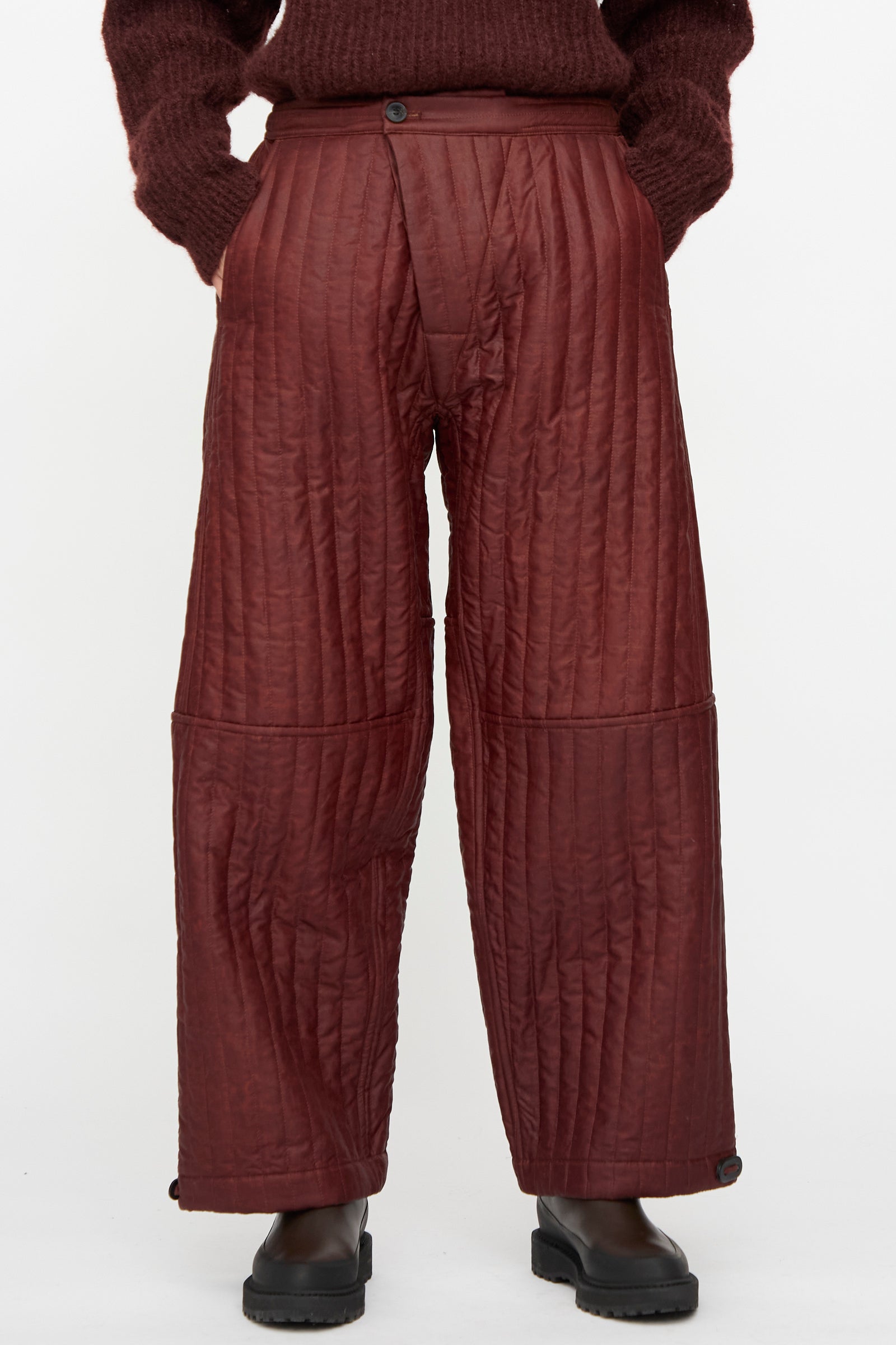 A person wears Jan-Jan Van Essche Shuliang Silk Padded Trousers #89 in Oxblood with a matching maroon sweater and black boots, standing against a plain white background.