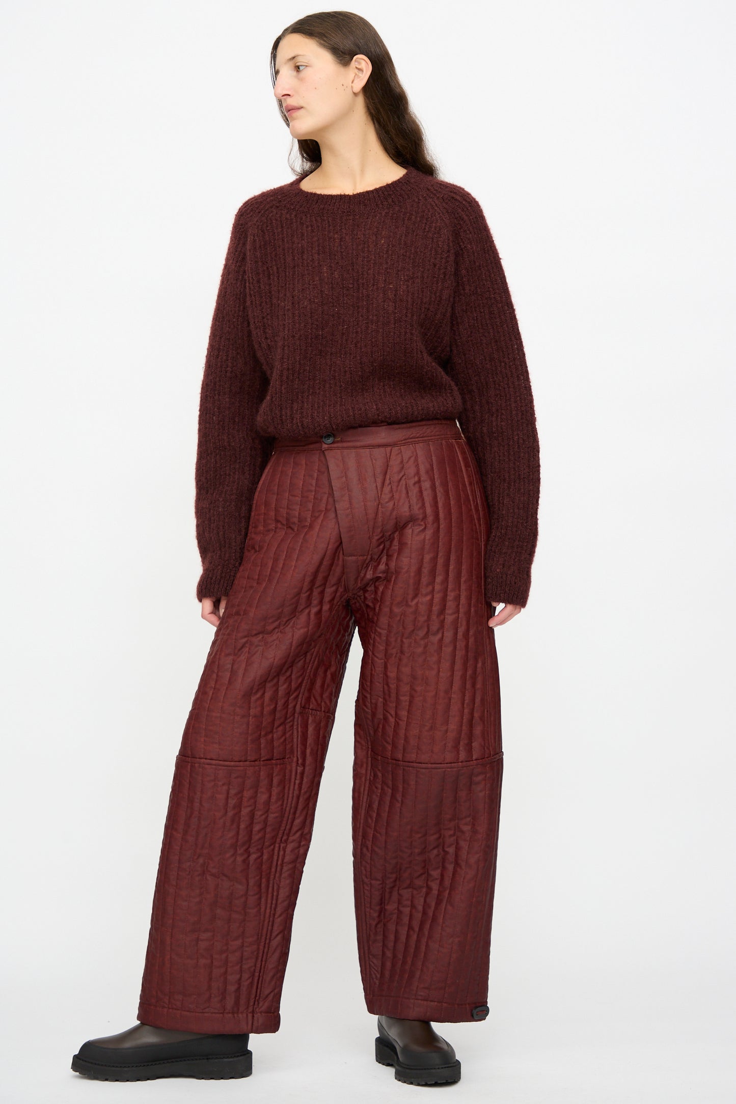 A person wears the Jan-Jan Van Essche Shuliang Silk Padded Trousers #89 in Oxblood with a maroon knit sweater and black shoes, standing against a plain white background.