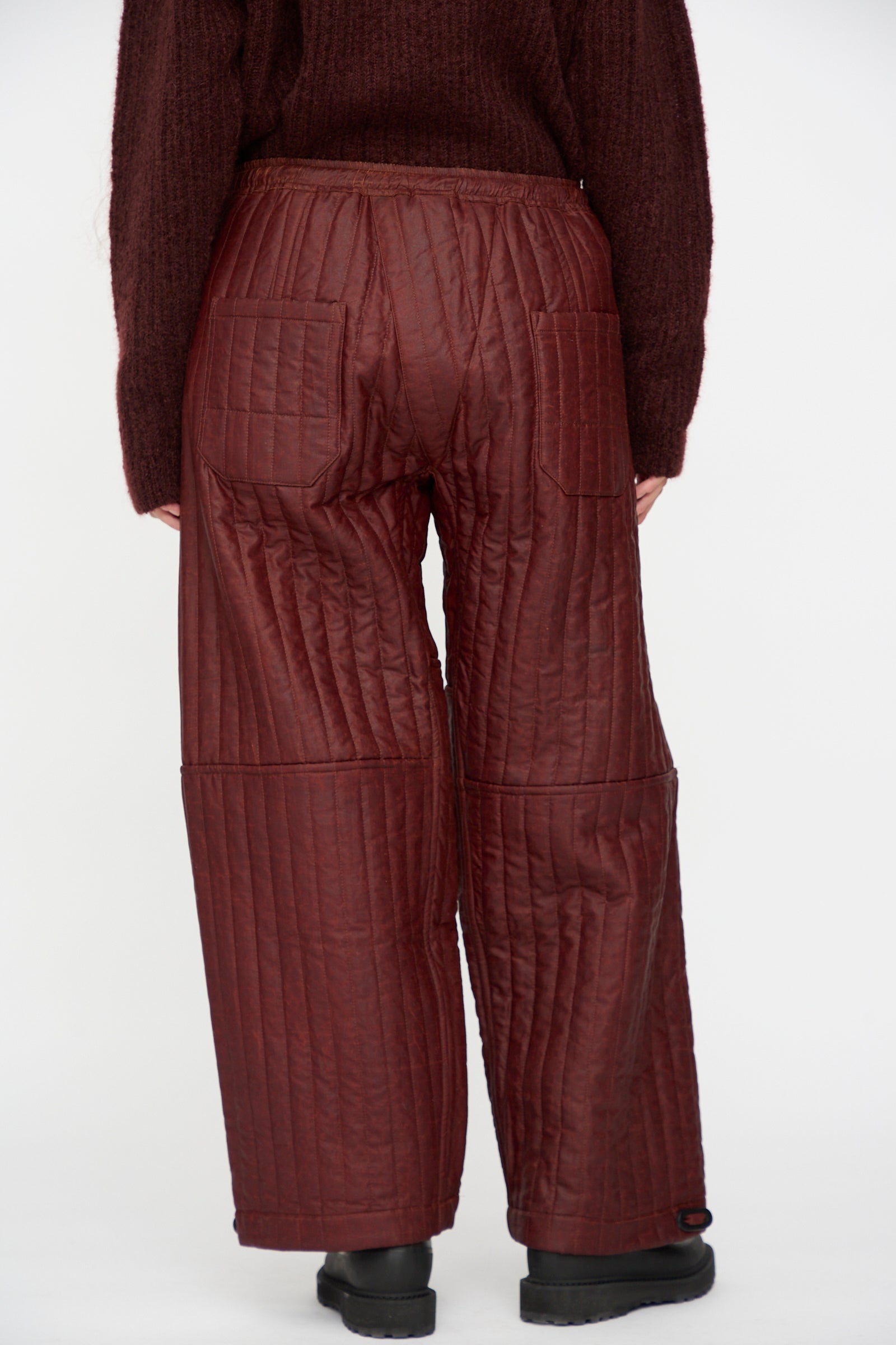 Person wearing Jan-Jan Van Essche Shuliang Silk Padded Trousers #89 in Oxblood, shown from the back with a matching sweater, standing against a plain white background.