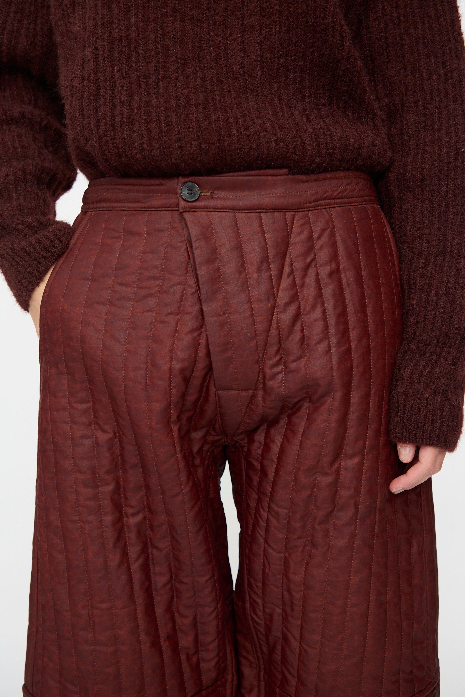 Model wearing Jan-Jan Van Essche's Shuliang Silk Padded Trousers #89 in Oxblood with relaxed fit and vertical quilting, one hand in the pocket; shown from mid-torso to mid-thigh.