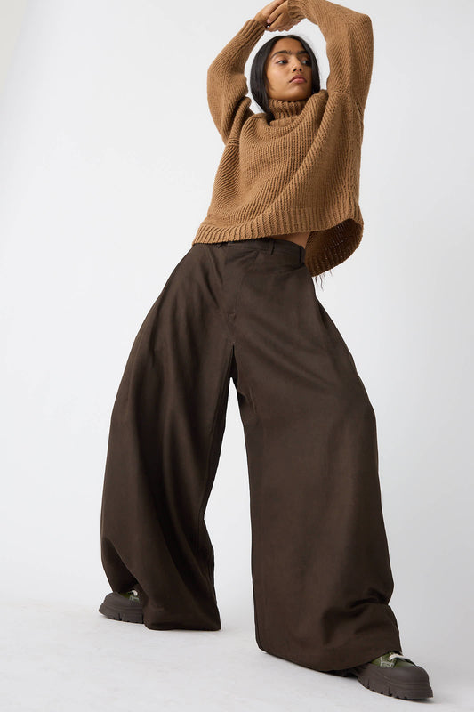 A person wearing a baggy sweater and the Jan-Jan Van Essche Silk Wool Twill Trouser in Amami Mud poses with arms raised.