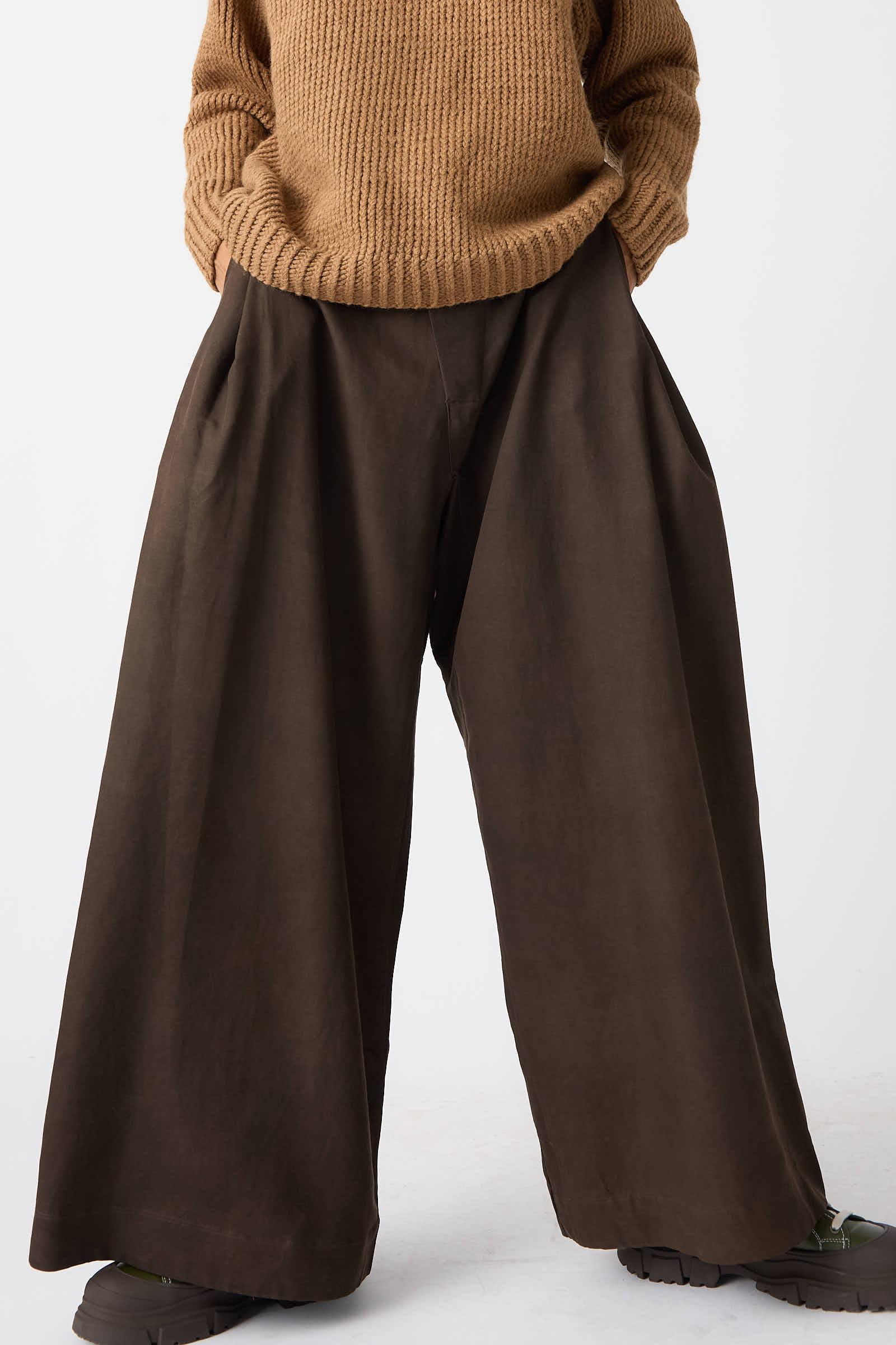 A person wearing a beige sweater, Jan-Jan Van Essche Silk Wool Twill Trousers in Amami Mud, and black shoes stands against a plain background.