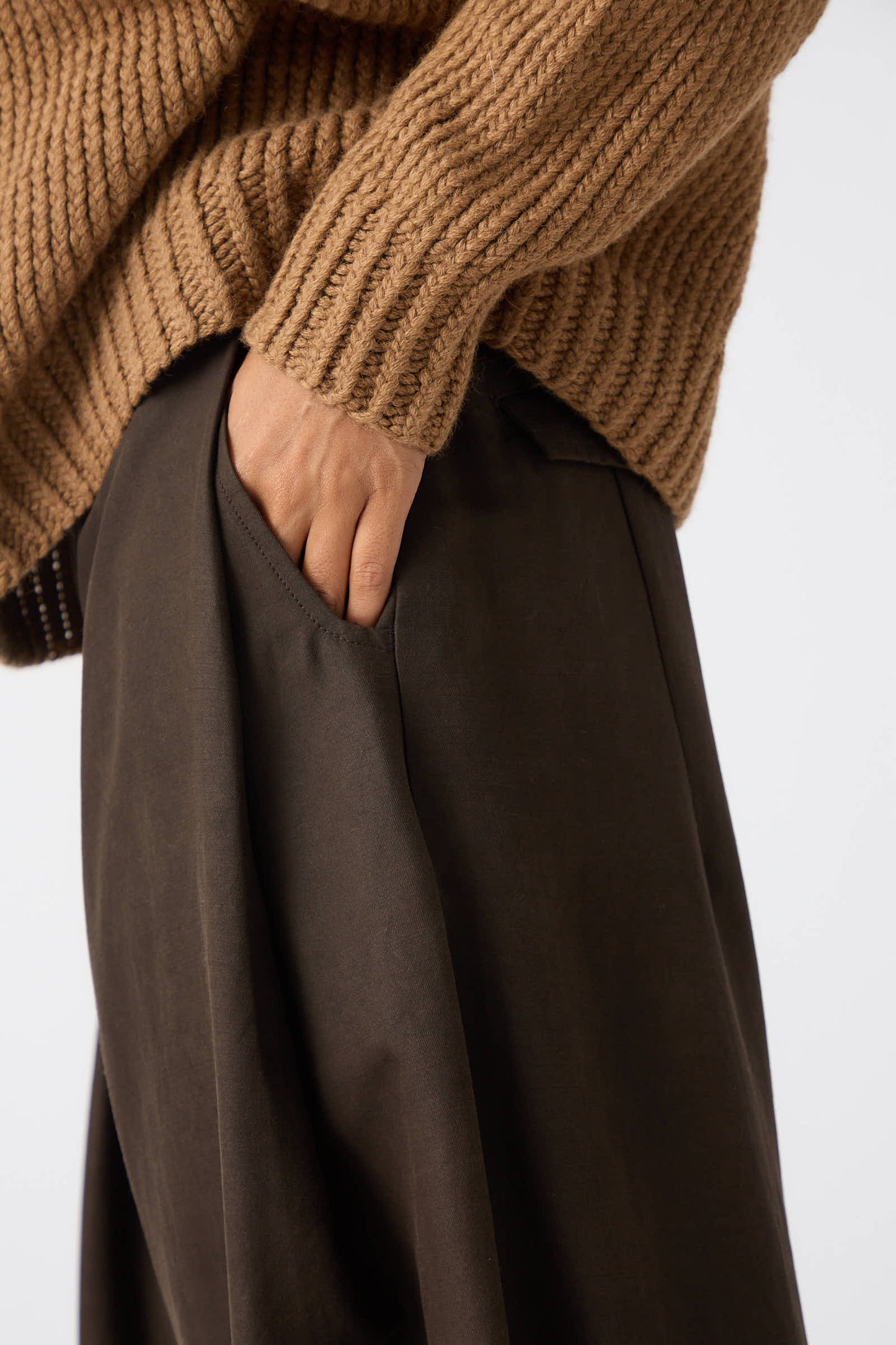 A person wearing a tan knit sweater and relaxed fit black Silk Wool Twill Trousers in Amami Mud by Jan-Jan Van Essche with their hand in their pocket.