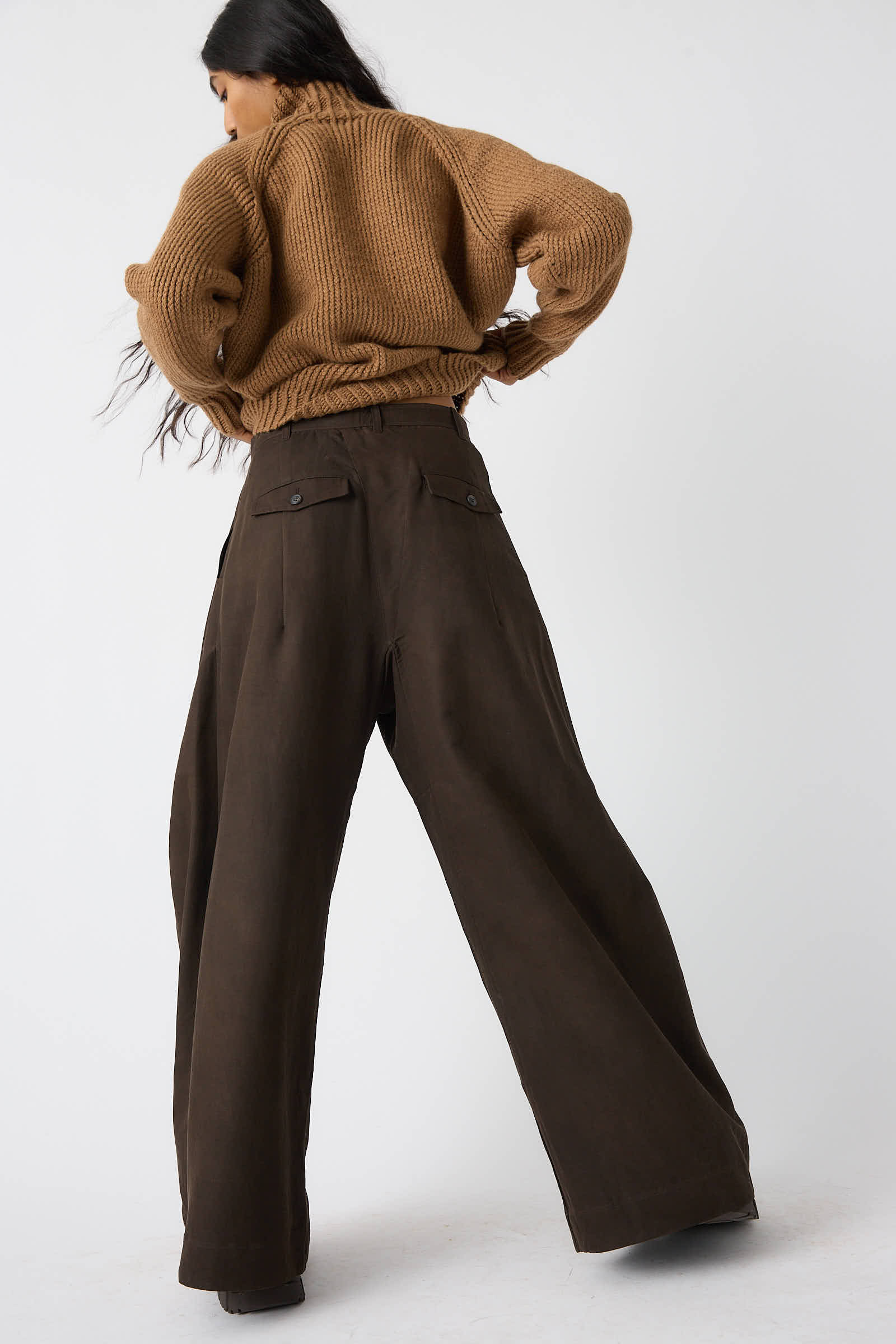 Person wearing a brown sweater and the Jan-Jan Van Essche Silk Wool Twill Trouser in Amami Mud, posing with their back to the camera against a plain background.