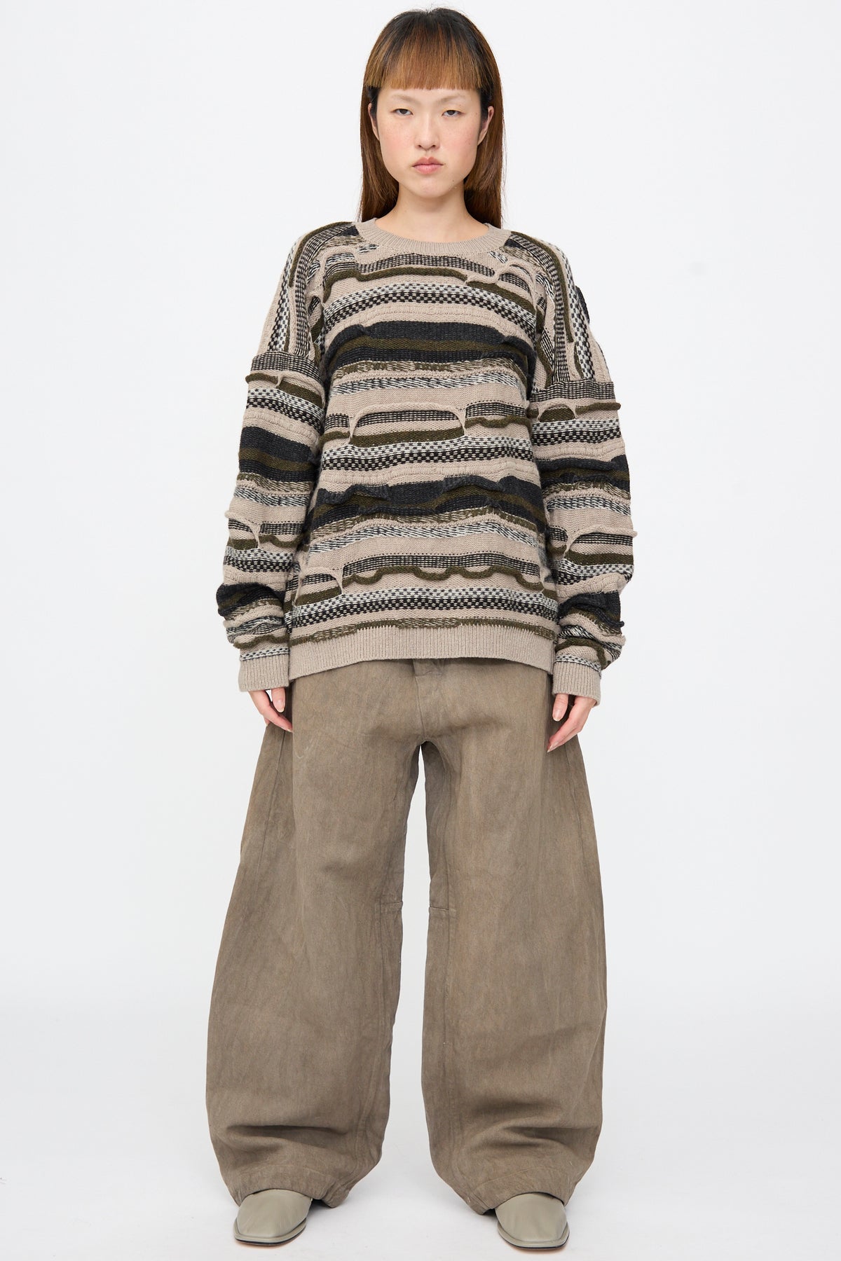 A Jan-Jan Van Essche Super Fine Wool Knit Sweater #80 in Light Variation, featuring an oversized, multi-textured, striped knit, worn with wide-leg trousers.