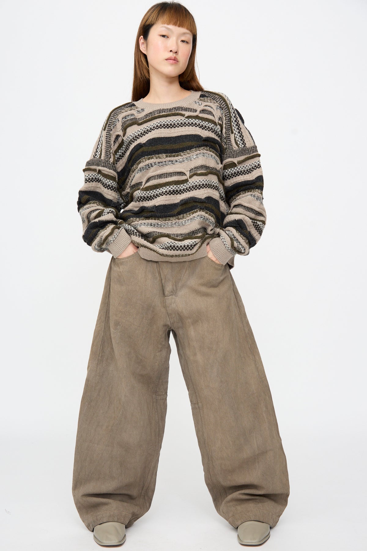 Person wearing a Jan-Jan Van Essche Super Fine Wool Knit Sweater #80 in Light Variation with a brown, green, and cream horizontal striped design and wide-leg trousers.