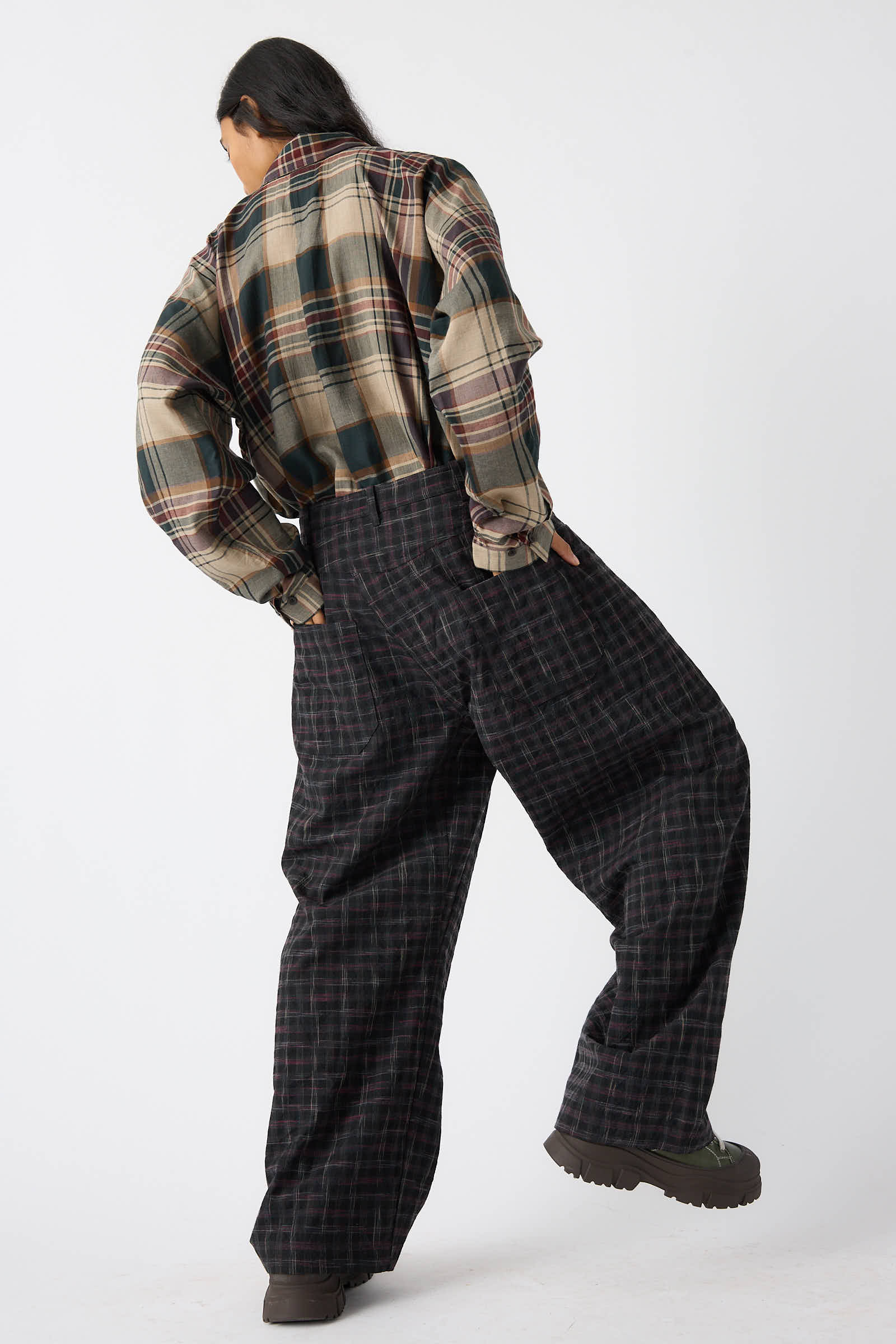 Person wearing an oversized plaid shirt and relaxed fit, Jan-Jan Van Essche Tumbled Wool Check Trouser in Kasuri, with hair tied back, standing with their back to the camera.