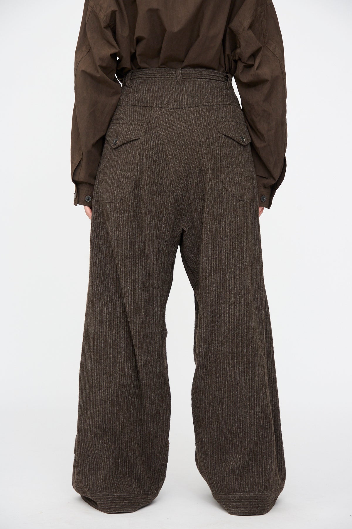 Rear view of a person wearing Yak Linen Cotton Trousers #93 in Brown Striped with buttoned back pockets and a matching dark brown shirt.