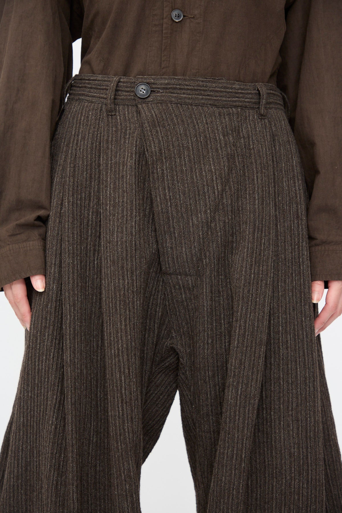Jan-Jan Van Essche Yak Linen Cotton Trousers #93 in Brown Striped featuring a double-pleated extra wide cut and button fly, worn with a brown long-sleeved shirt.
