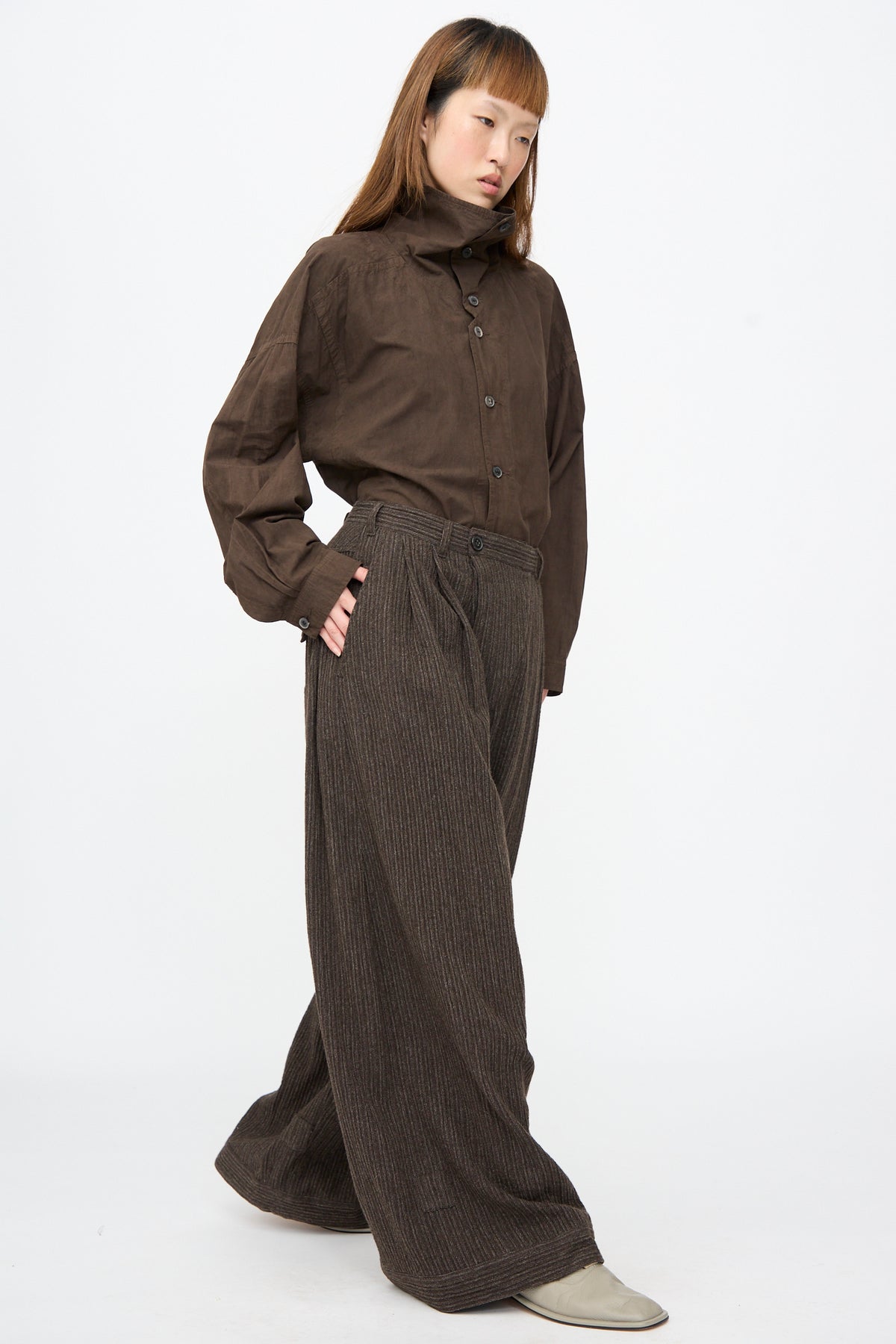 A person wears a dark brown button-down shirt tucked into Jan-Jan Van Essche Yak Linen Cotton Trousers #93 in Brown Striped, featuring an extra wide fit and double pleated front.