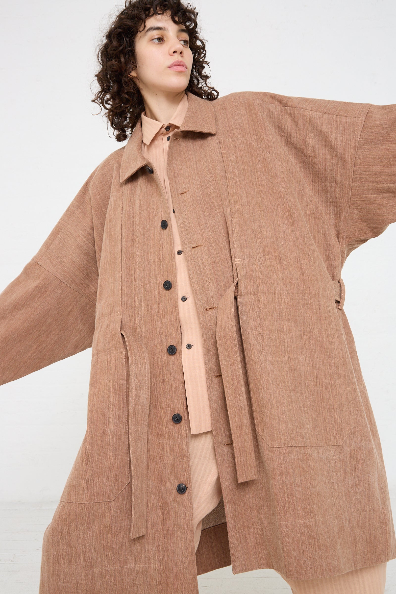 The model is wearing a Jan-Jan Van Essche Woven Cotton Long Coat in Kakishibu with a self tie belt.