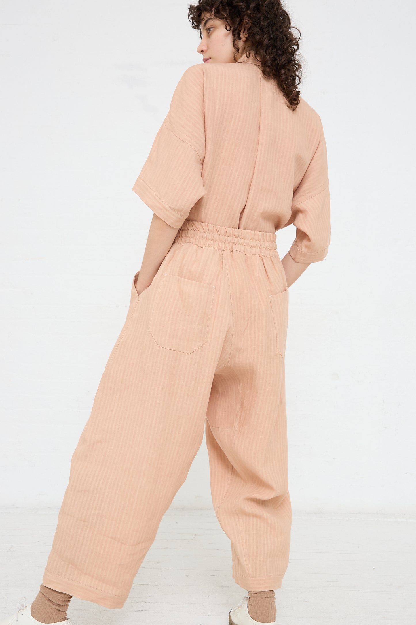 The model is wearing a woven linen trouser in Ume (Pink) by Jan-Jan Van Essche. Full length and back view.