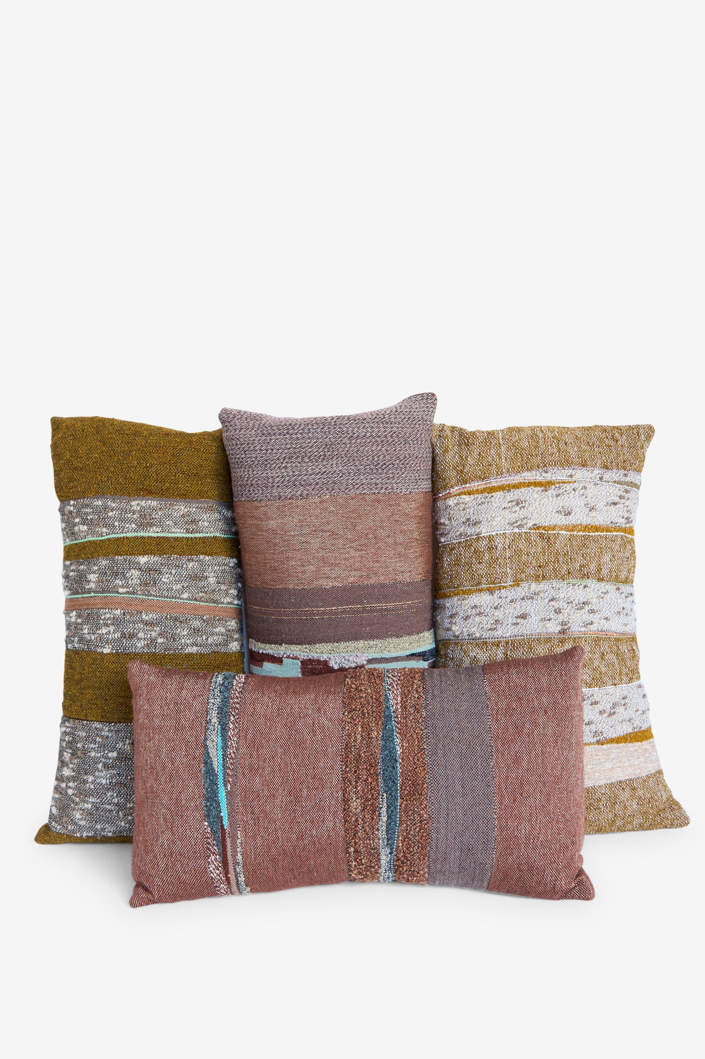 Four Jess Feury Handwoven Rock Slab Pillows in Topaz and Copper, made from sustainable fibers, feature earth toned stripes and are stacked against a white background.