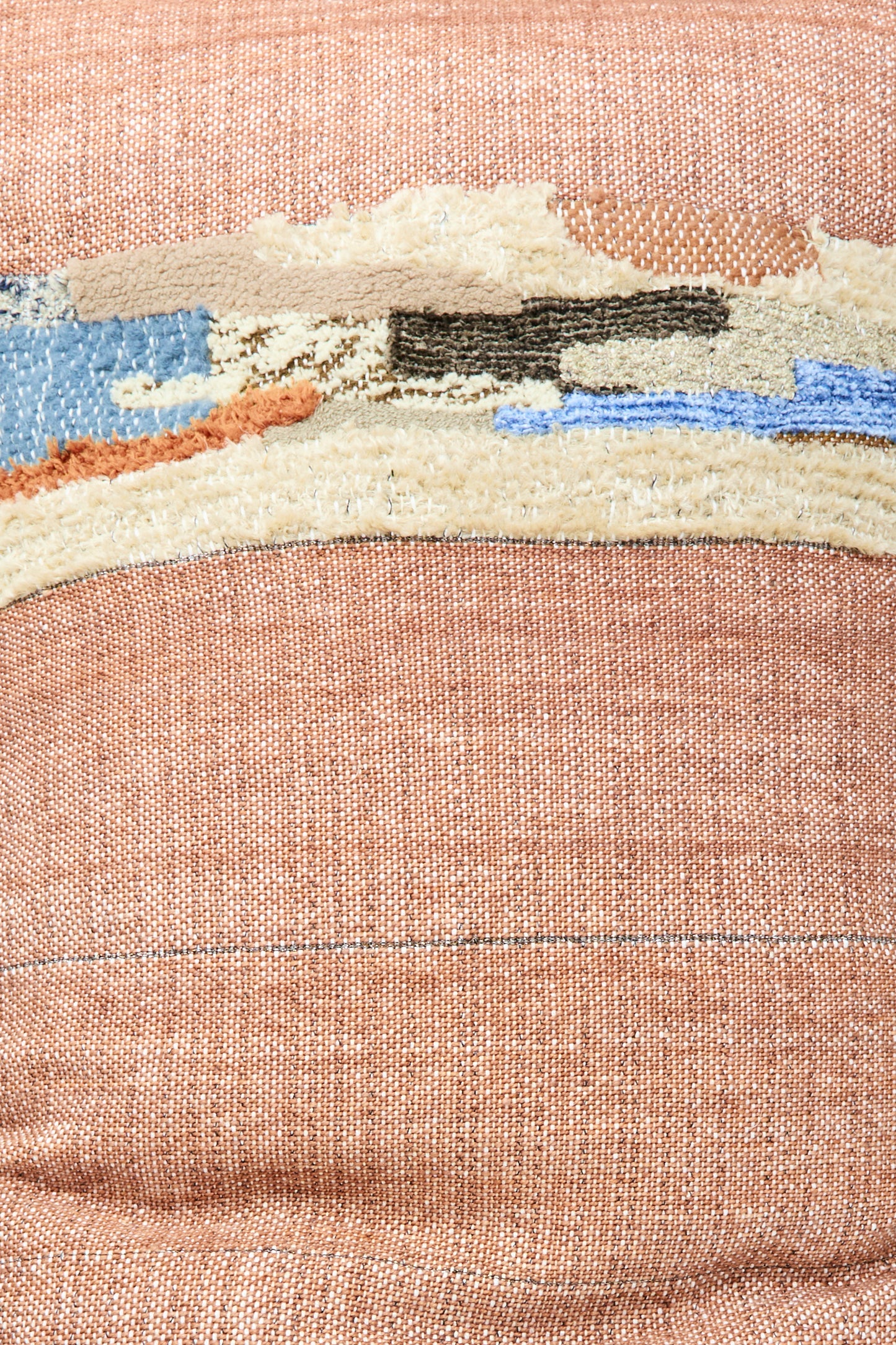 A close-up of the Jess Feury Woven Colorblock Pillow in Persimmon and Clay, featuring an abstract embroidered design in beige, blue, brown, and cream on a muted pink fabric, handmade in California.