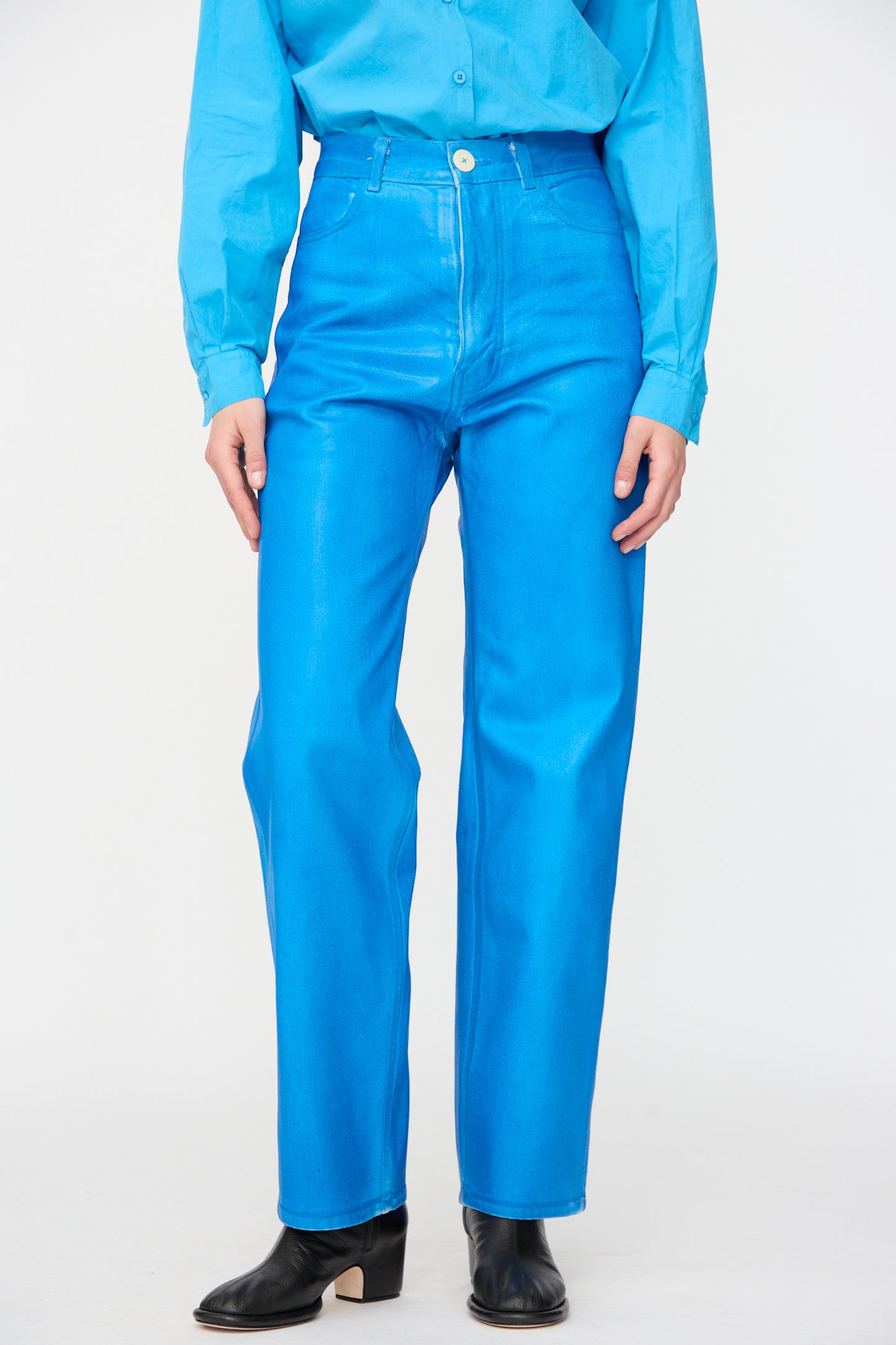 Wearing Jesse Kamm's 225 Jeans in Electric Blue Lacquer, styled with a matching long-sleeve shirt and black ankle boots, standing with hands by their sides.