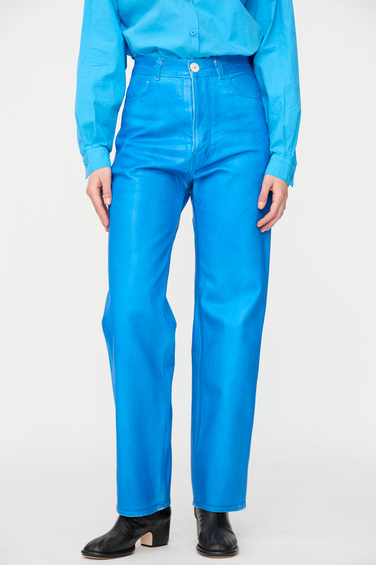 Wearing Jesse Kamm's 225 Jeans in Electric Blue Lacquer, styled with a matching long-sleeve shirt and black ankle boots, standing with hands by their sides.