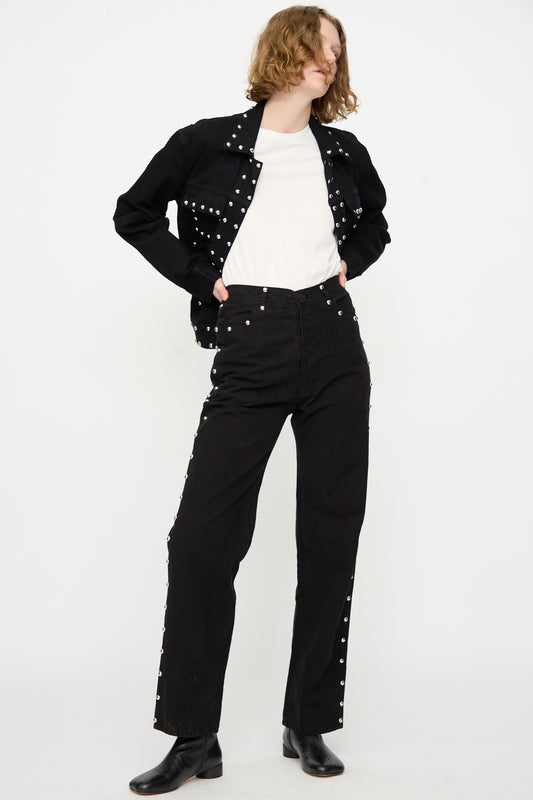 A person wearing Jesse Kamm’s 225′s in Black with Studs stands against a plain white background with hands on hips, styled with a high-rise pant, white shirt, and black boots.