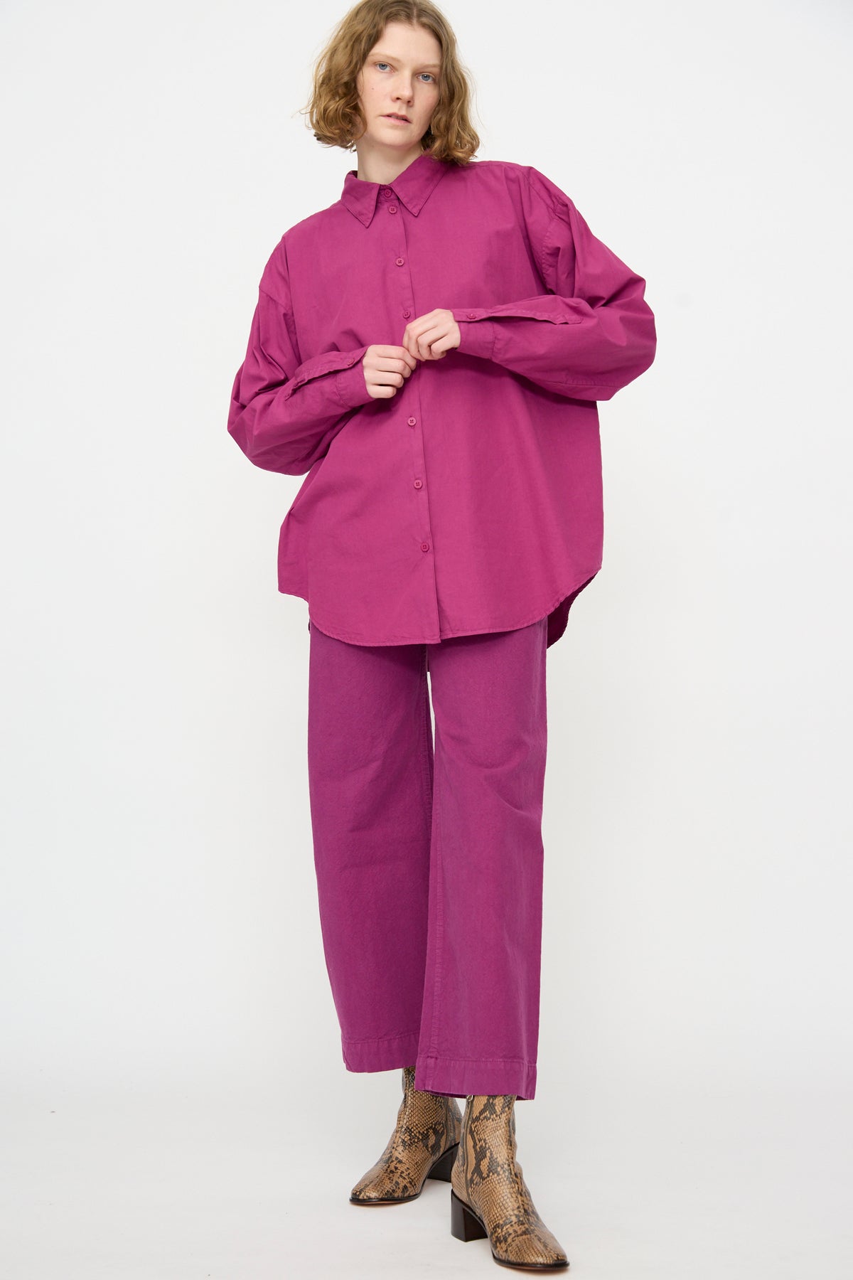 Person wearing an oversized fit, Jesse Kamm Alberta Shirt in Beet with matching pants and light brown snakeskin-patterned boots, standing against a plain white background.