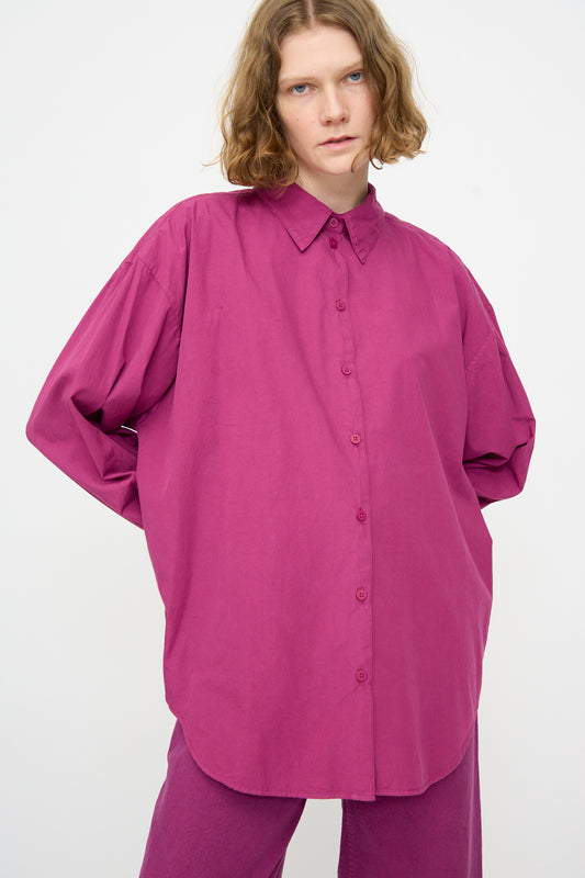 Person with shoulder-length wavy hair wearing the Jesse Kamm Alberta Shirt in Beet, styled loosely and oversized with matching pants, standing against a plain white background.