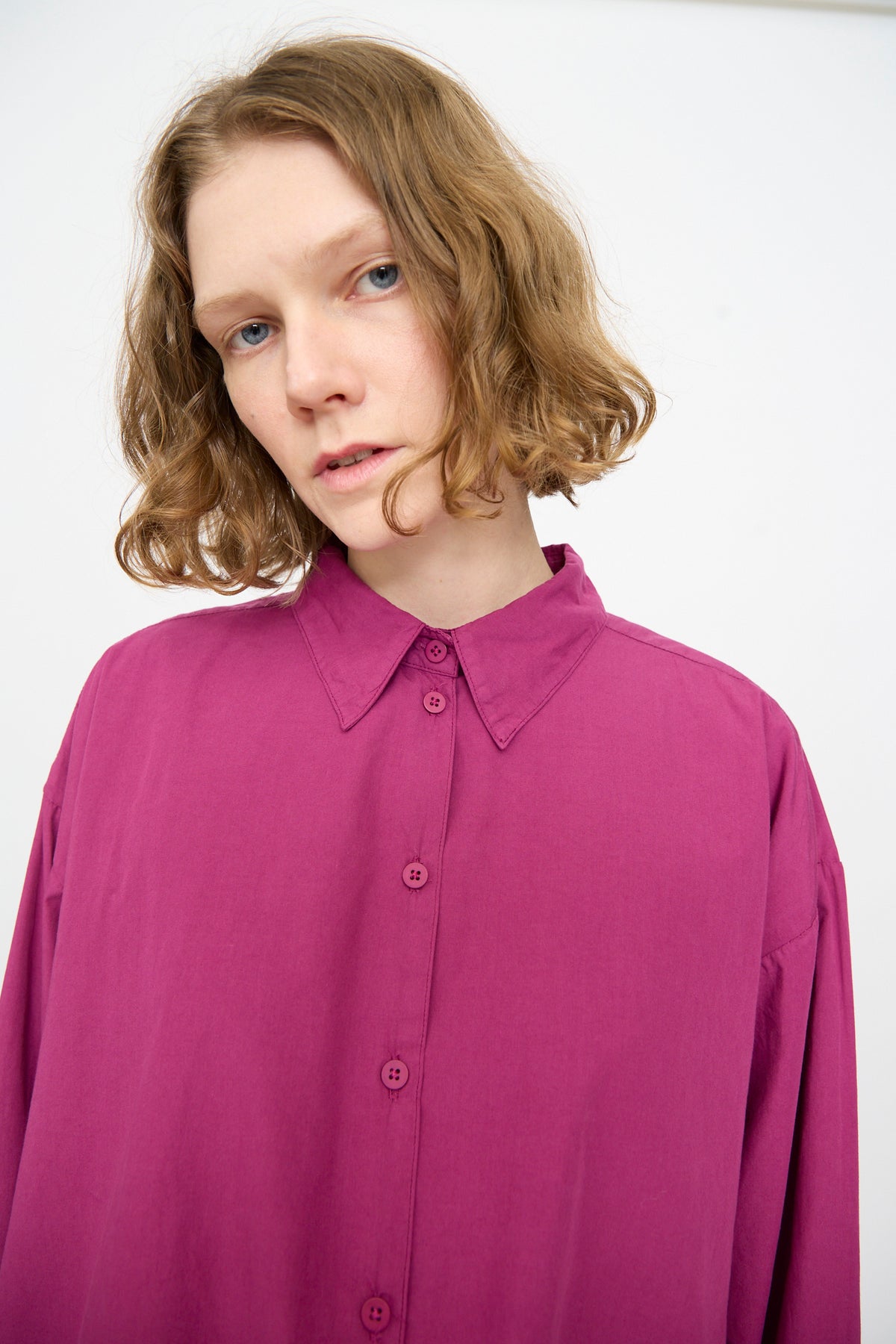 A person with short wavy hair wears the Jesse Kamm Alberta Shirt in Beet, an oversized fit button-up, standing against a plain white background.