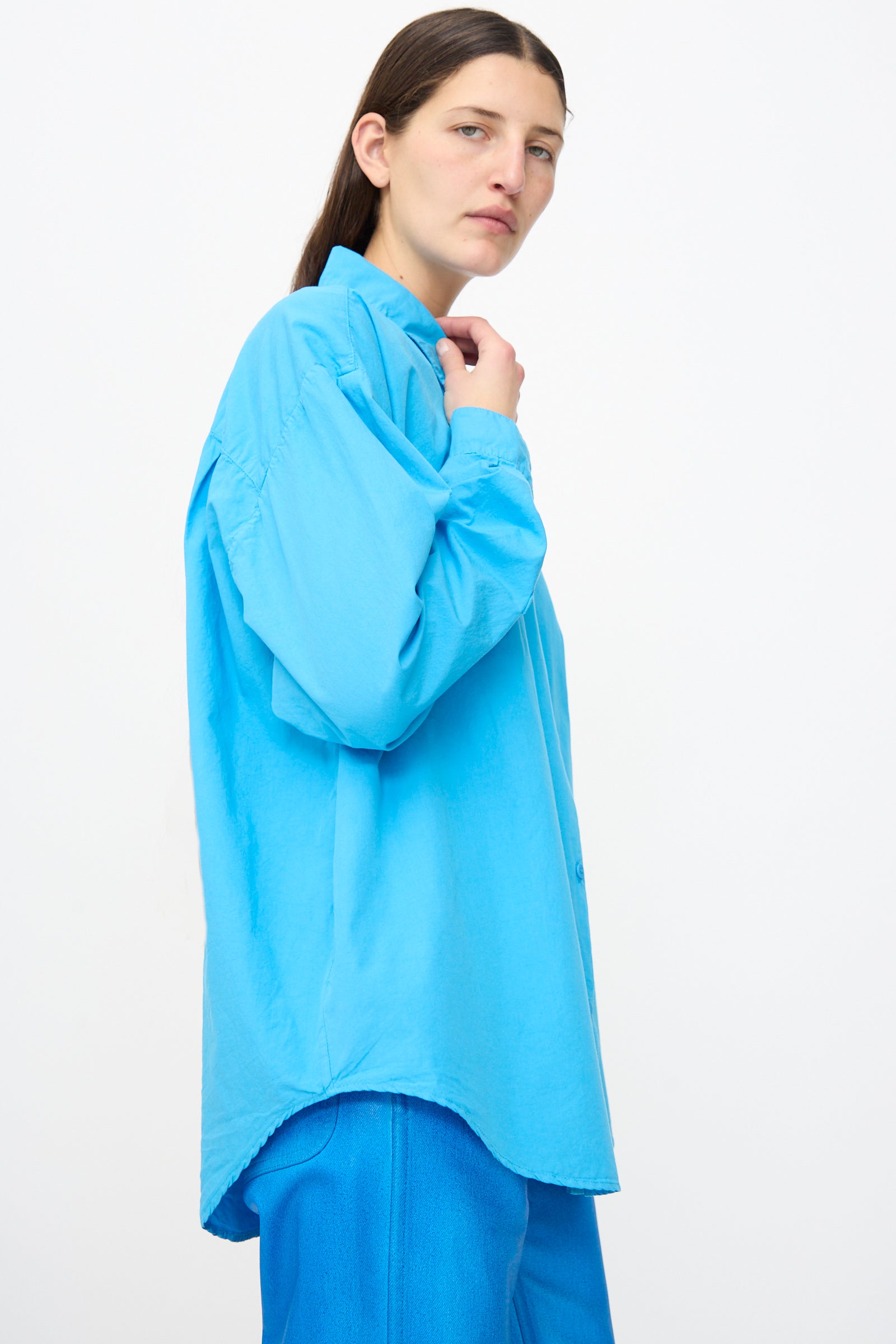 Model wears the Jesse Kamm Alberta Shirt in Pool Blue—crafted from organic cotton—in a loose fit with matching blue pants, standing against a plain white background.