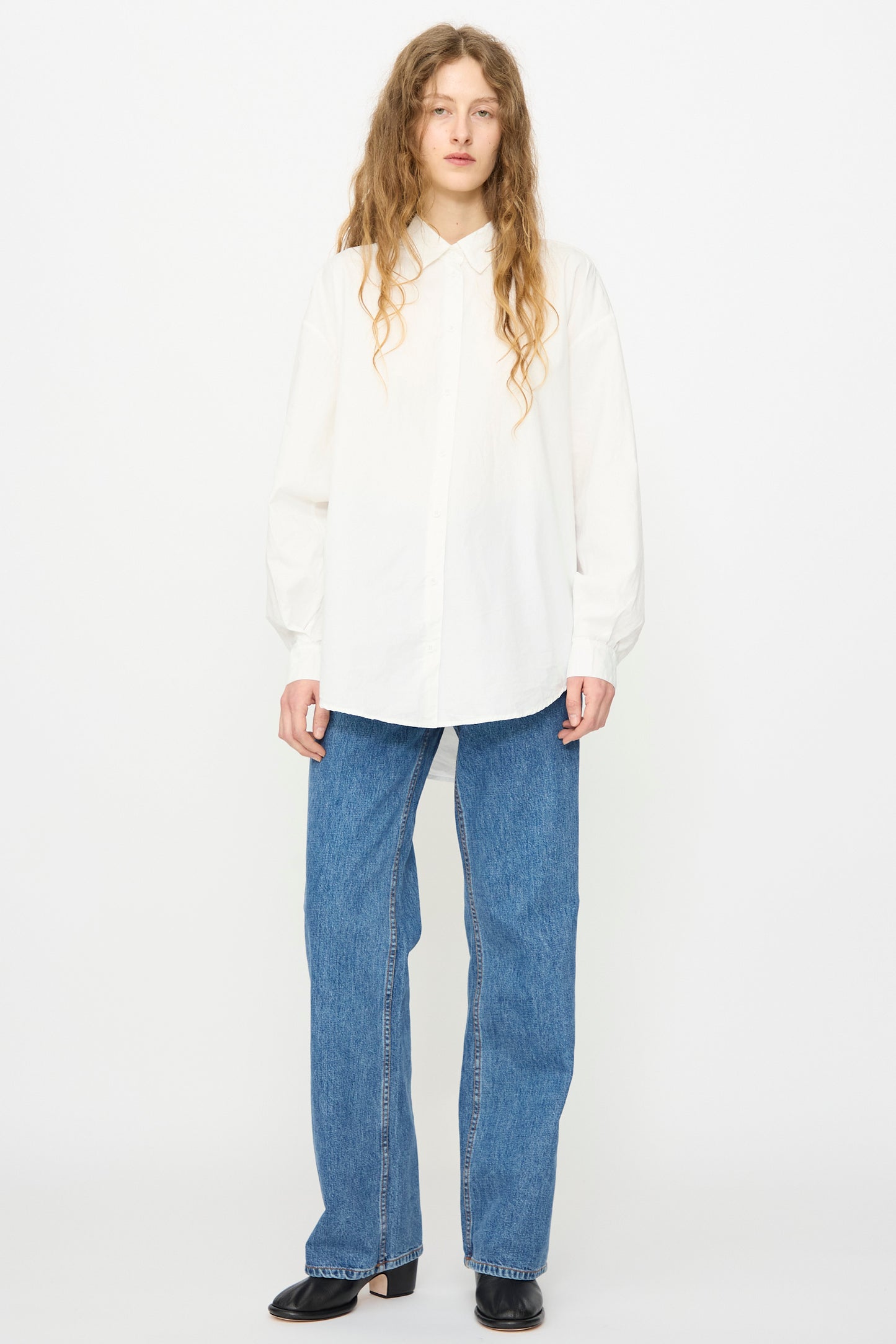 A person stands against a plain background wearing the Jesse Kamm Alberta Shirt in Salt White, paired with blue jeans and black shoes.