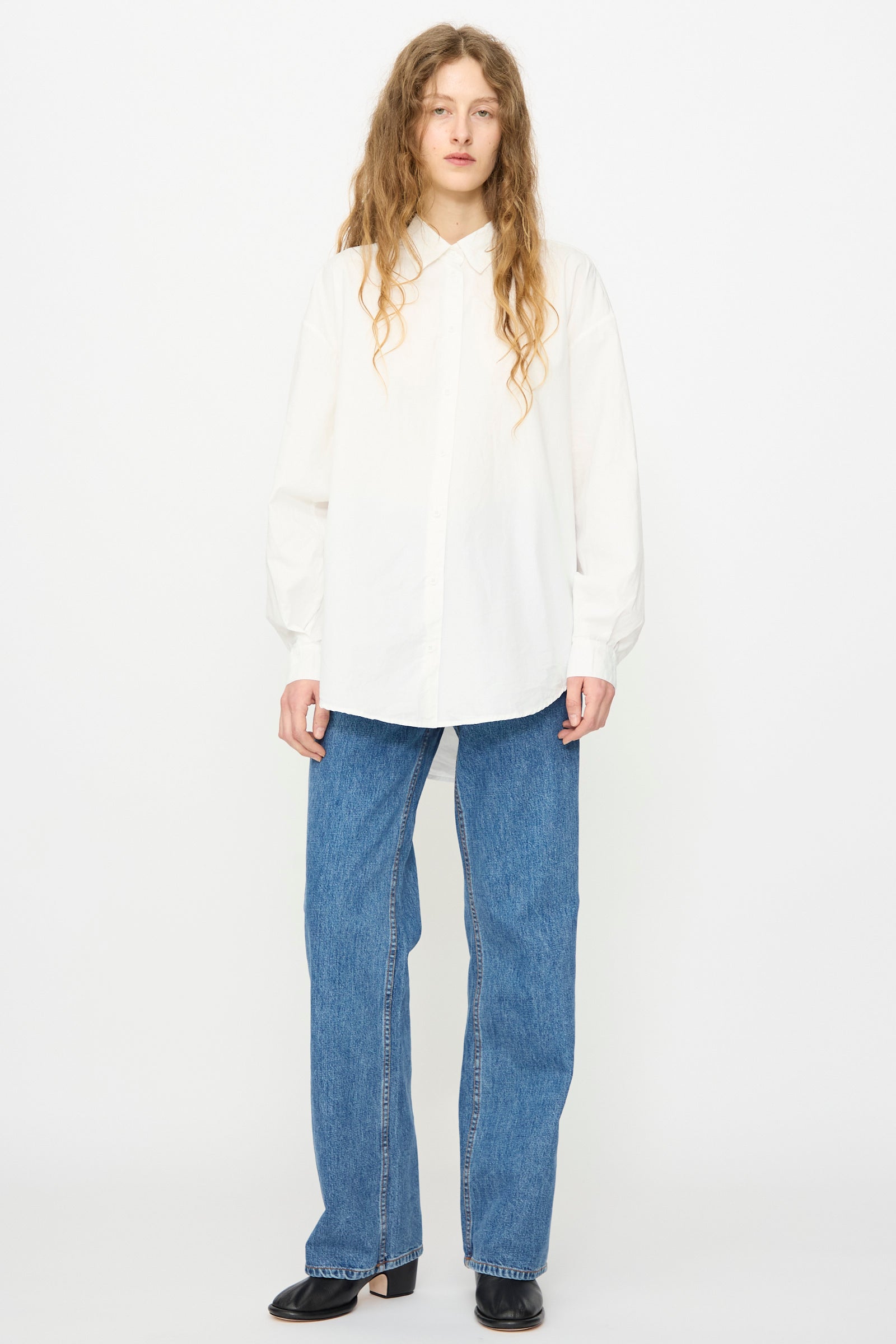 A person stands against a plain background wearing the Jesse Kamm Alberta Shirt in Salt White, paired with blue jeans and black shoes.
