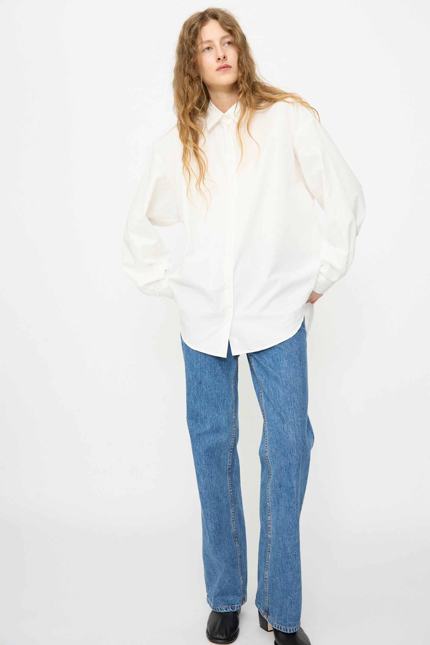 A person wears the Jesse Kamm Alberta Shirt in Salt White, paired with blue straight-leg jeans and black shoes, standing against a plain white background.