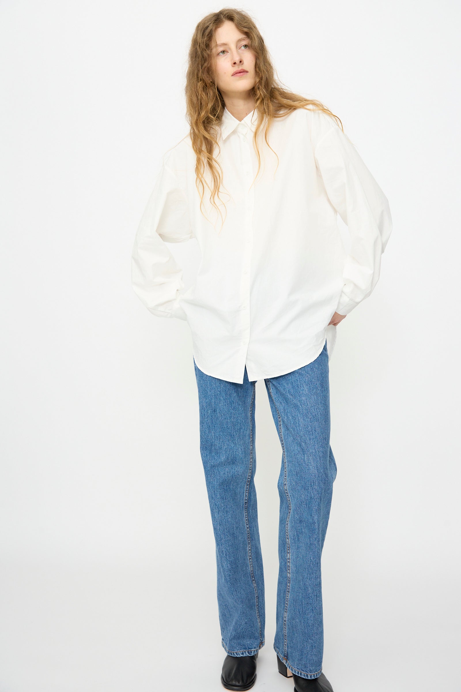 A person wears the Jesse Kamm Alberta Shirt in Salt White, paired with blue straight-leg jeans and black shoes, standing against a plain white background.