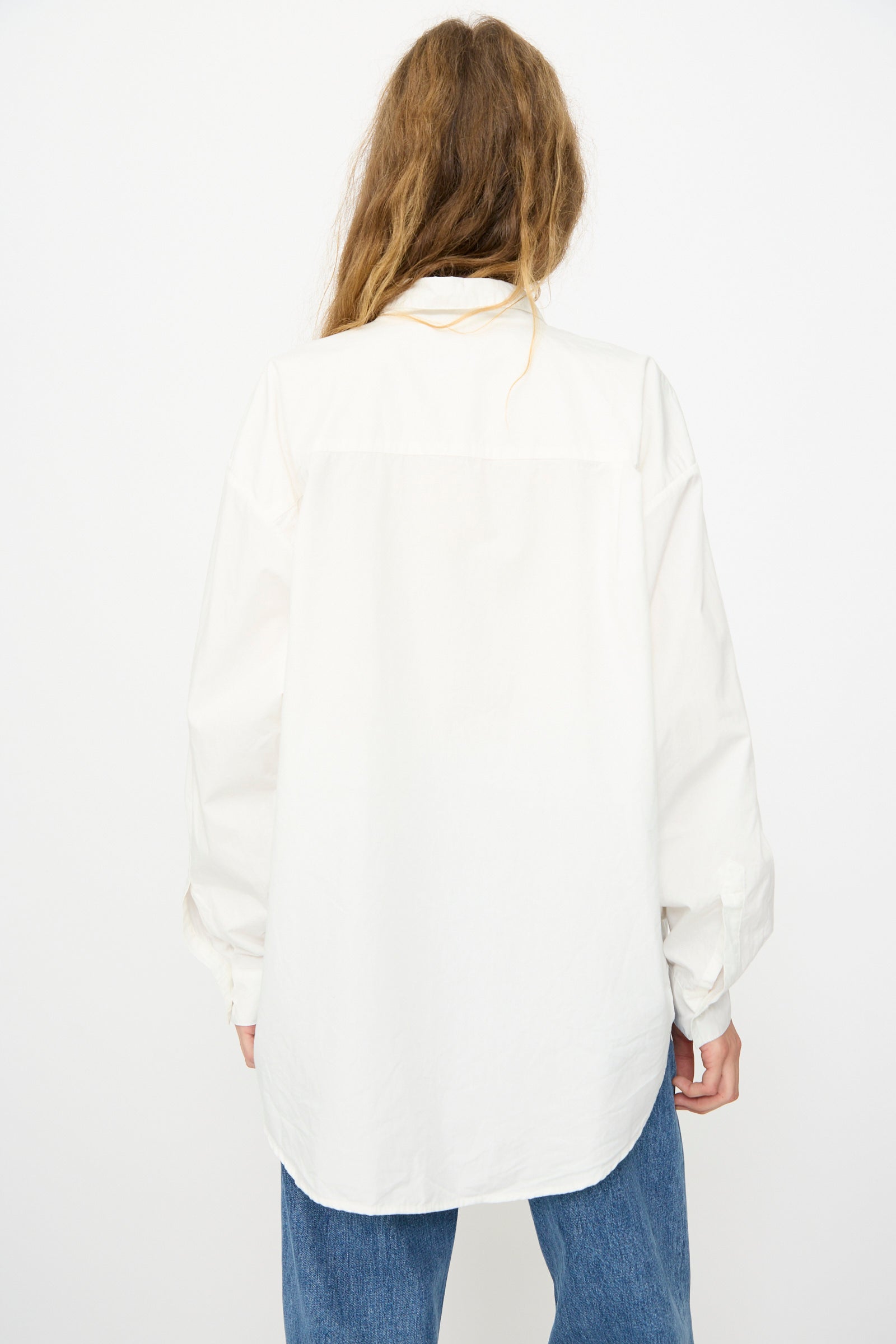 A person with long hair wears the Jesse Kamm Alberta Shirt in Salt White and blue jeans, standing with their back to the camera against a plain white background.