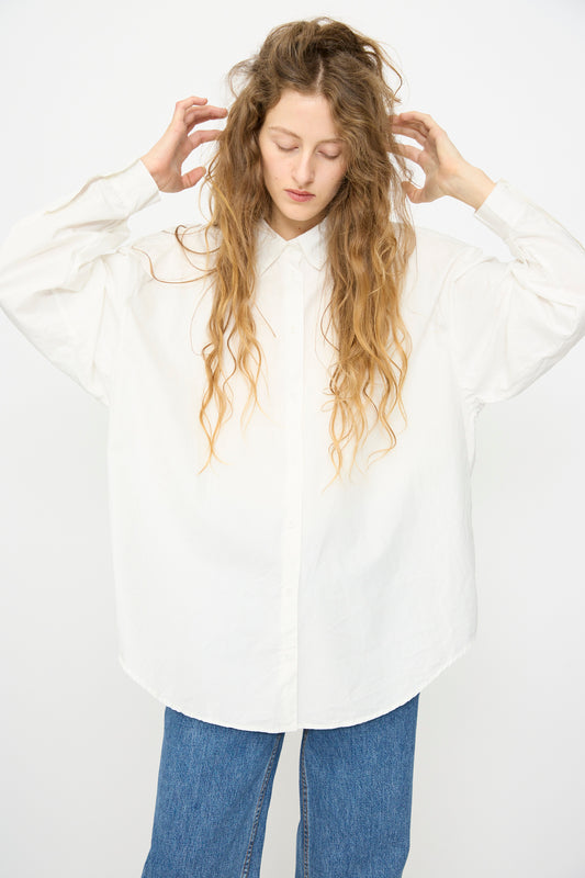 A person with long wavy hair wears the Jesse Kamm Alberta Shirt in Salt White and blue jeans, standing against a plain white background.