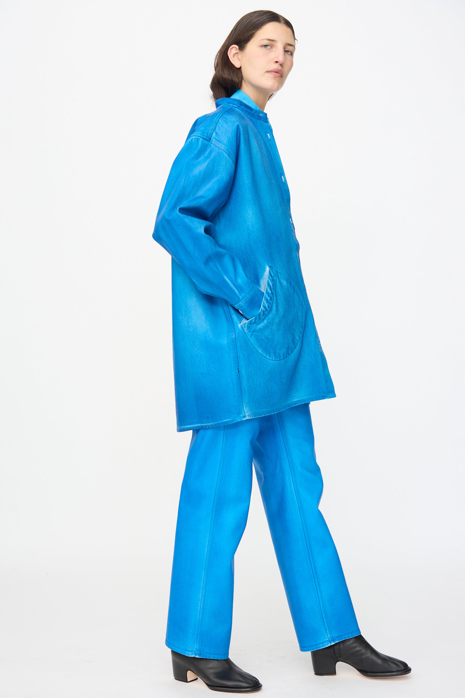 A person wears the Jesse Kamm Band Collar Okuda Jacket in Electric Blue Lacquer with matching pants and black heeled boots, standing against a plain white background.