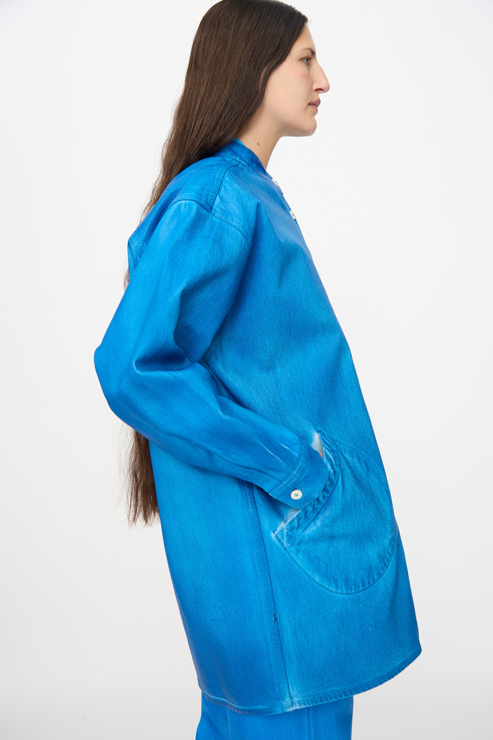 A person with long brown hair wears the Jesse Kamm Band Collar Okuda Jacket in Electric Blue Lacquer with matching pants, standing in profile against a plain white background.